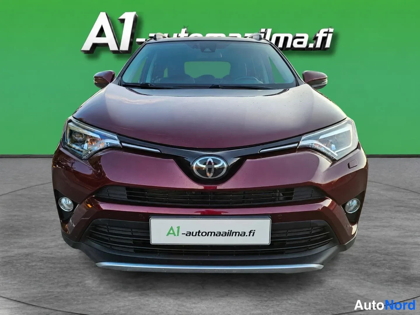 Edestä: Tummansininpunainen Toyota RAV4 suoraan edestä kuvattuna vihreää studioseinää vasten.