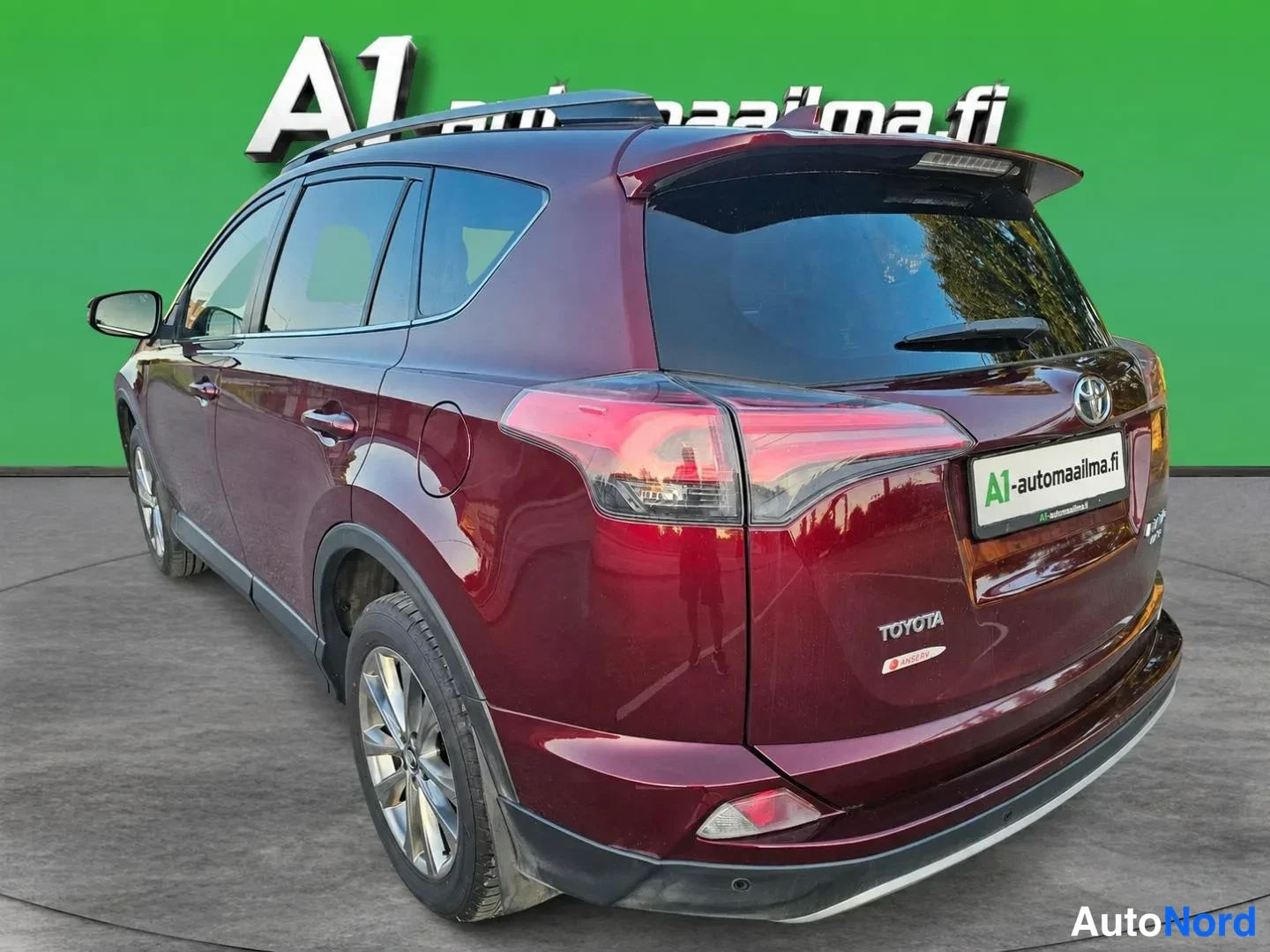 Takaviisto: Tummansininpunainen Toyota RAV4 takavasemmalta kolmannelta neljännekseltä kuvattuna vihreää studioseinää vasten.