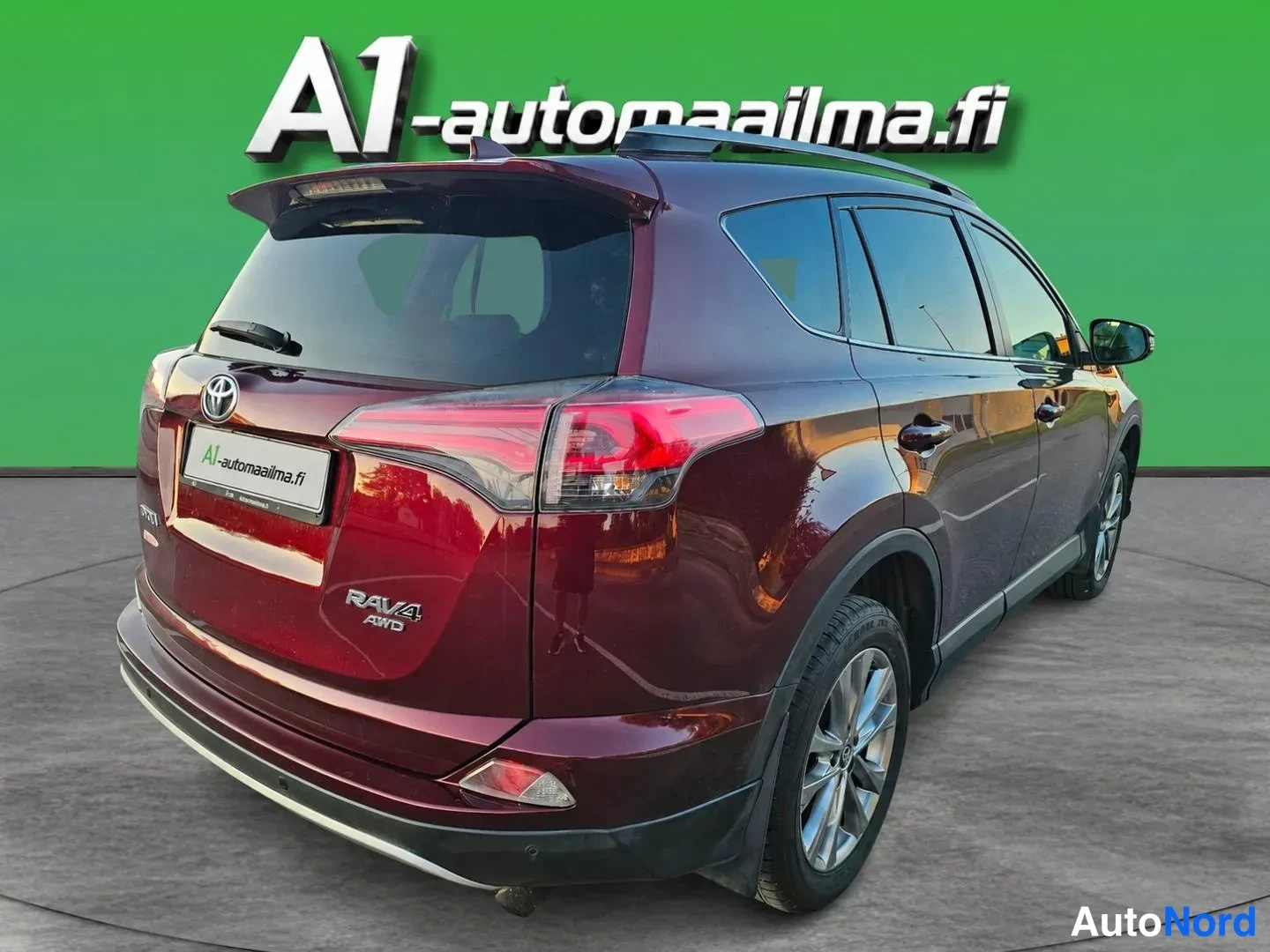 Takaviisto: Takakulmanäkuva tummanpunaisesta Toyota RAV4 -maasturista, jossa näkyvät takavalot, kohoumessa oleva Toyota-merkki, RAV4 AWD -teksti, kattokaiteet ja takarenkai