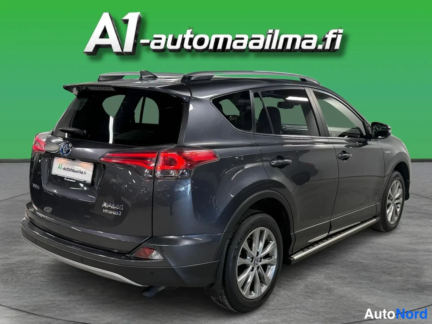 Takaviisto: Taka kolmasosan kuvakulma vasemmasta takakulmasta: tummanharmaa Toyota RAV4 Hybrid, kattokaiteet, hologattu kylki ja kevytmetallivanteet näkyvät.