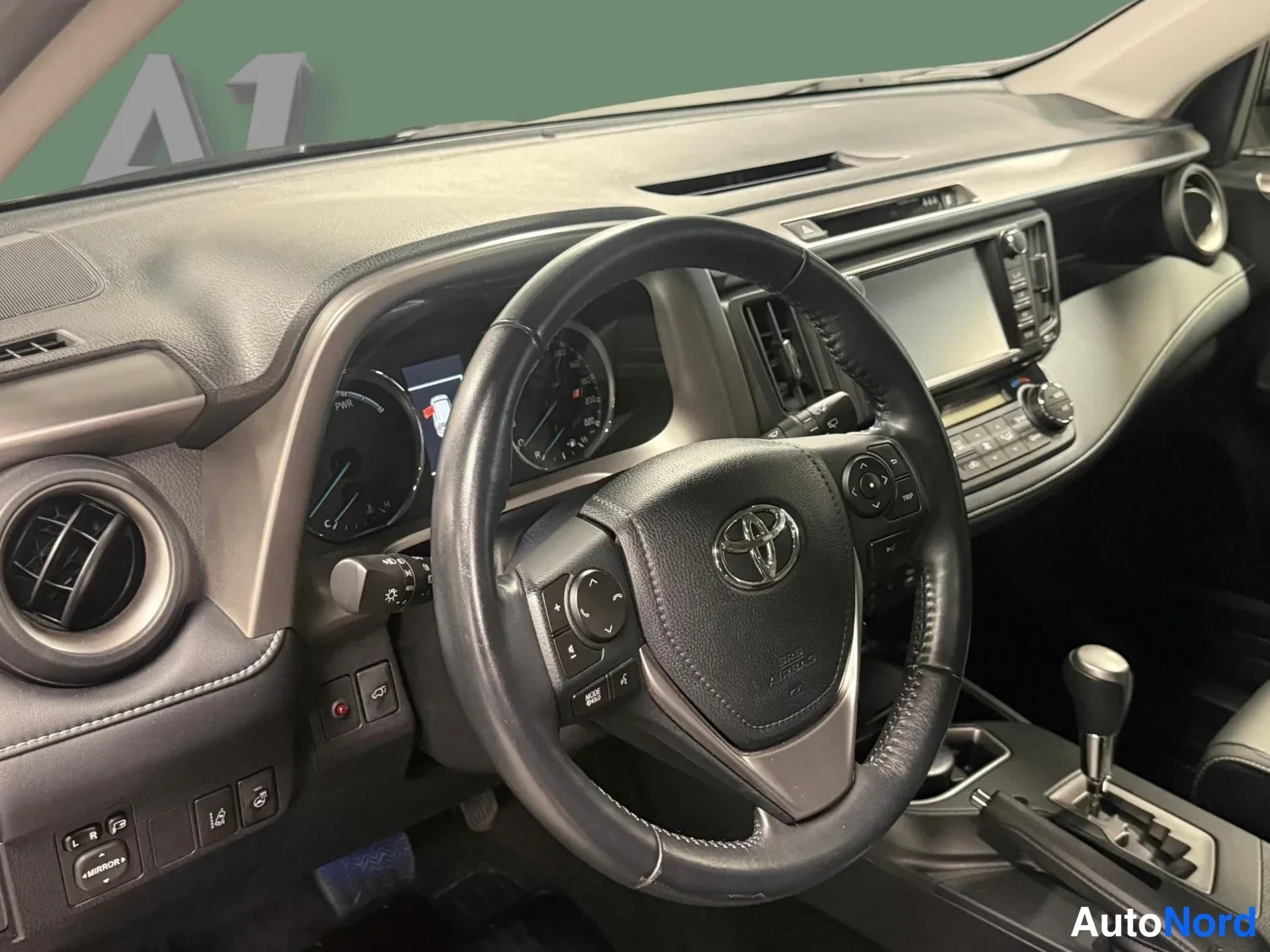 Muu: Lähikuva ohjauspyörästä ja kojelautaa: Toyota-merkitty ohjauspyörä, digitaalinen mittaristo ja kosketusnäyttö keskellä.