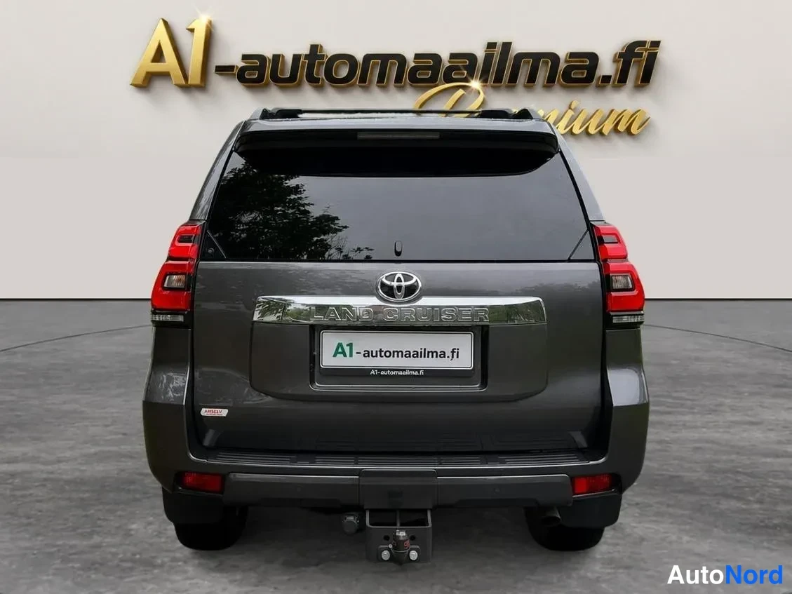 Takaa: Toyota Land Cruiserin takaosa suoraan takaa; tummanharmaa kori, LAND CRUISER-teksti, Toyota-merkki ja vetokoukku takapuskissa.