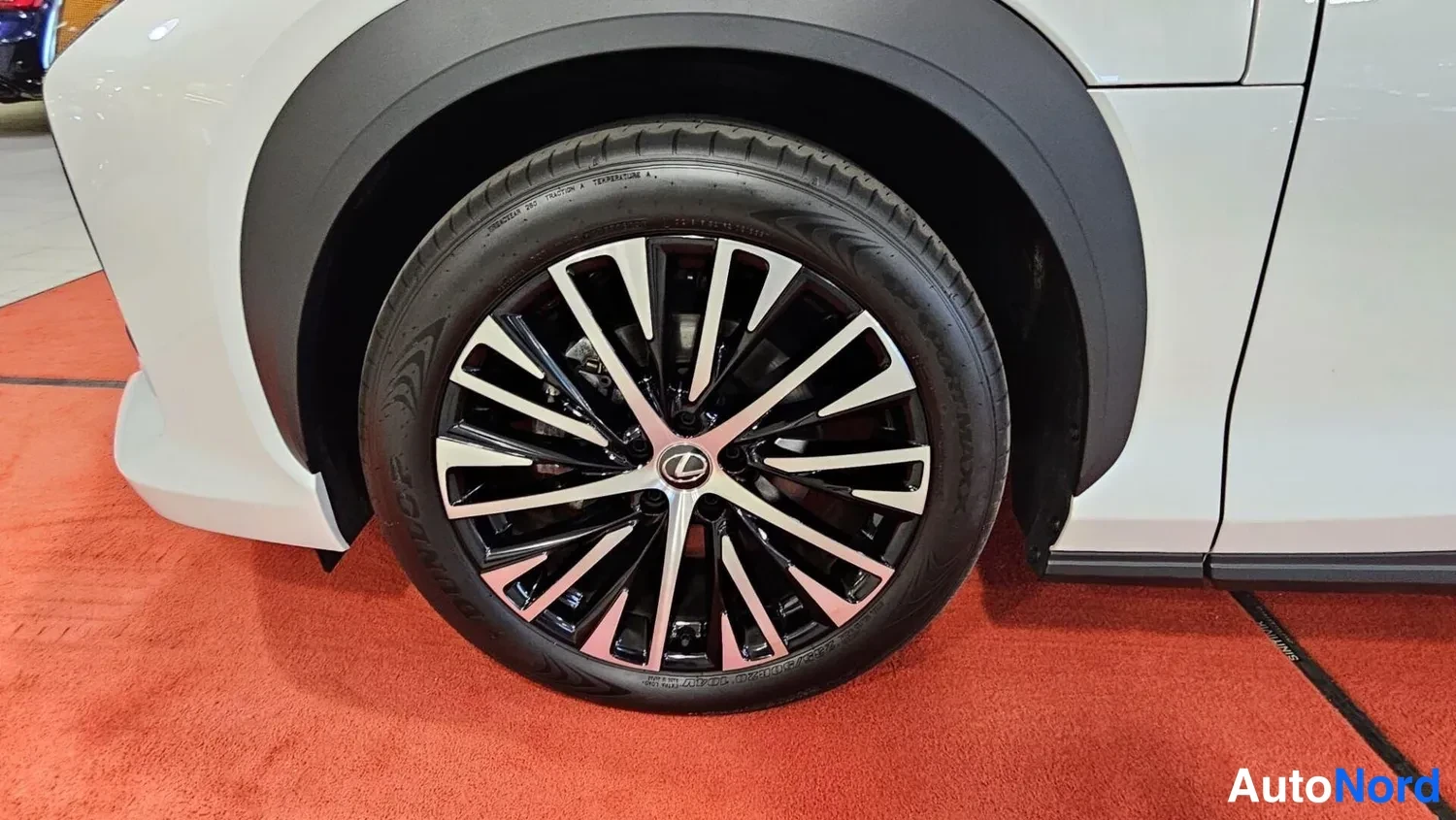 Sivulta: Auton pyörä ja etulokasuoja lähikuvassa; hopeanvalkoinen runko ja musta levykeväxallinen vanteen keskellä Lexus-merkki.