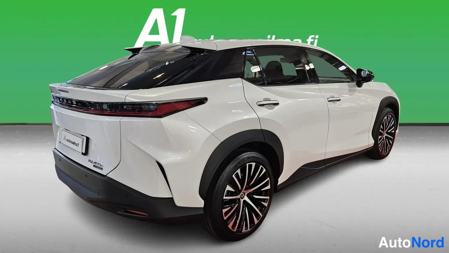Takaviisto: White Lexus RZ photographed from a rear three-quarter angle, showing the tail light bar, boot lid with Lexus lettering, rear wheel, doors and glass roof in fron