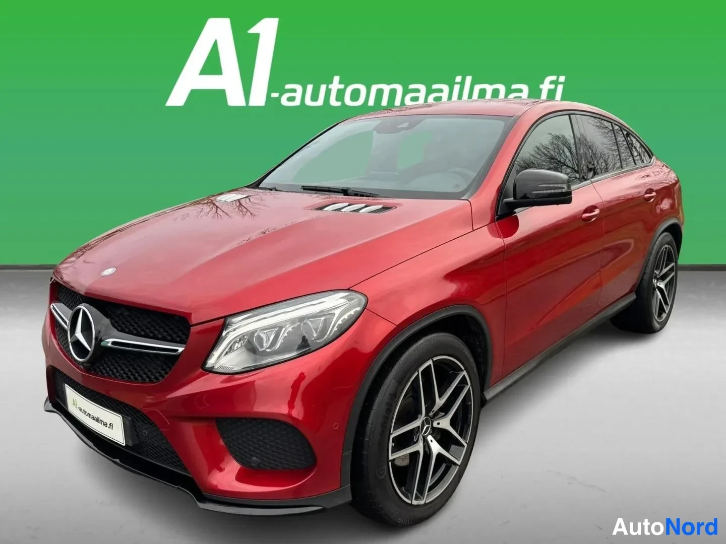 Etuviisto, nokka vasemmalle: Punainen Mercedes-Benz GLE Coupé kolmasosan etunäkymässä vihreää taustaa vasten; etusäleikkö, ajovalot ja mustat kevytmetallivanteet näkyvät.