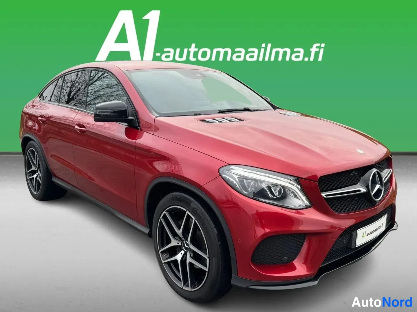 Etuviisto, nokka oikealle: Punainen Mercedes-Benz GLE Coupé etukulmasta oikealta vihreää taustaa vasten; ajoneuvon etuosa ja kylki näkyvät, mustat kevytmetallivanteet erottuvat.