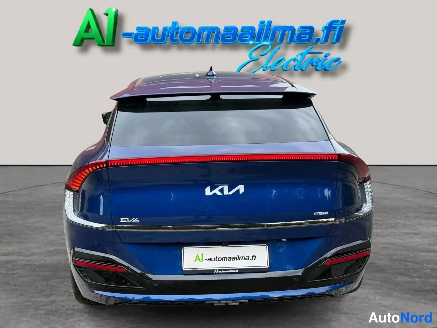 Takaa: Sininen Kia EV6 takaa kuvattuna; kokonaislevittävä punainen takavaloaukko, Kia-merkki ja EV6-teksti takaluukussa.