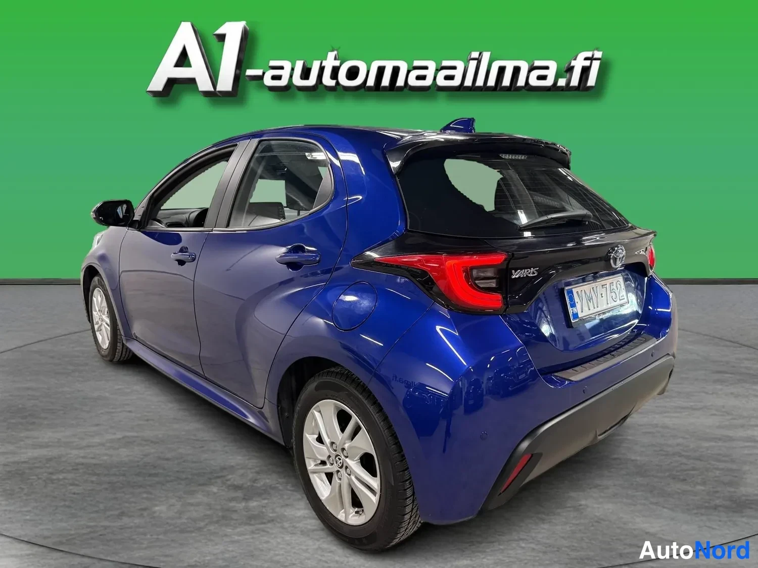 Takaviisto: Sininen Toyota Yaris -henkilöauto taka- ja sivusta kolmeneljäsosan kuvakulmasta, tunnus.
