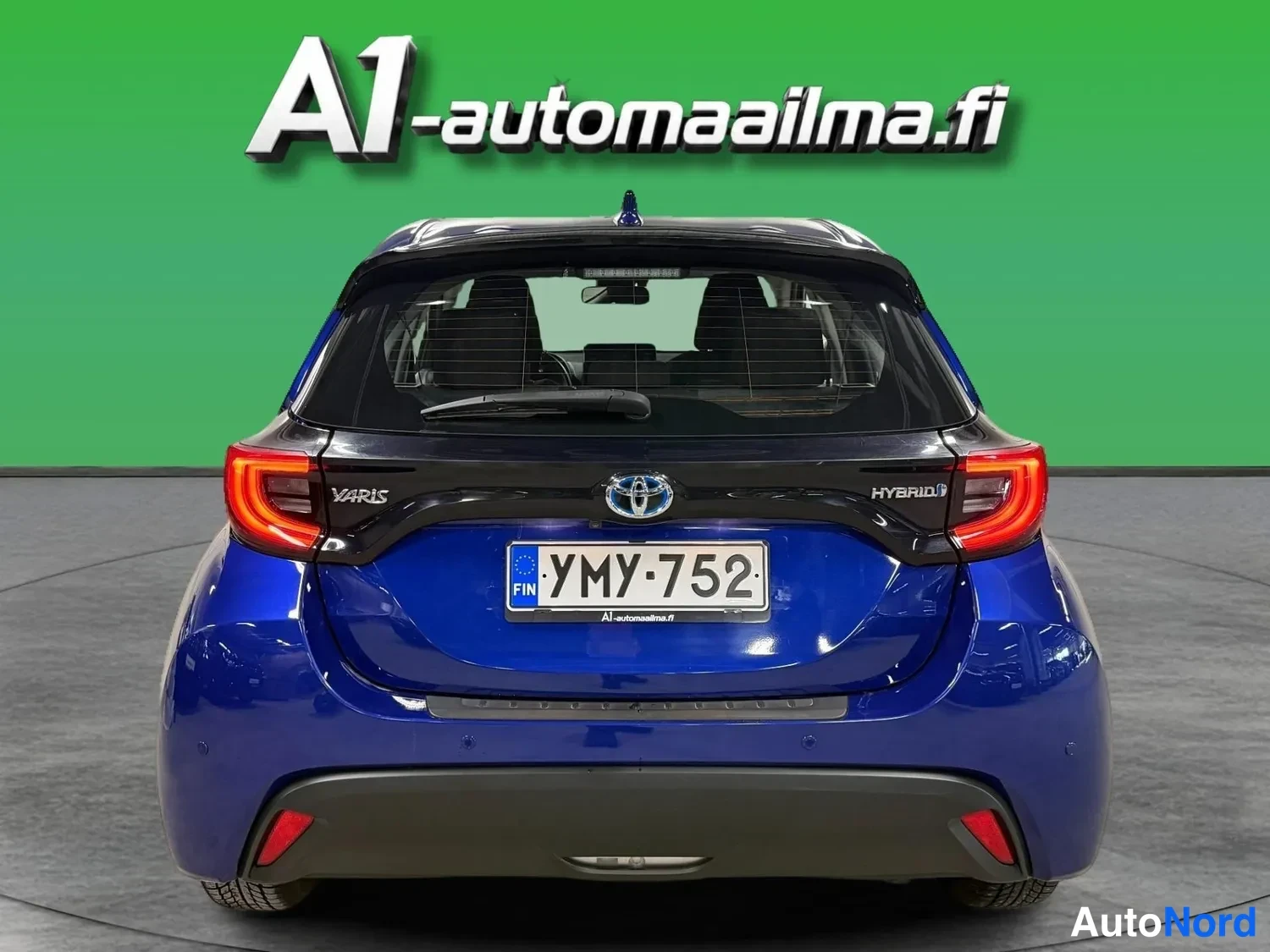 Takaa: Sininen Toyota Yaris takaa: rekisterikilpi, Hybrid-merkintä ja Toyota-merkki.