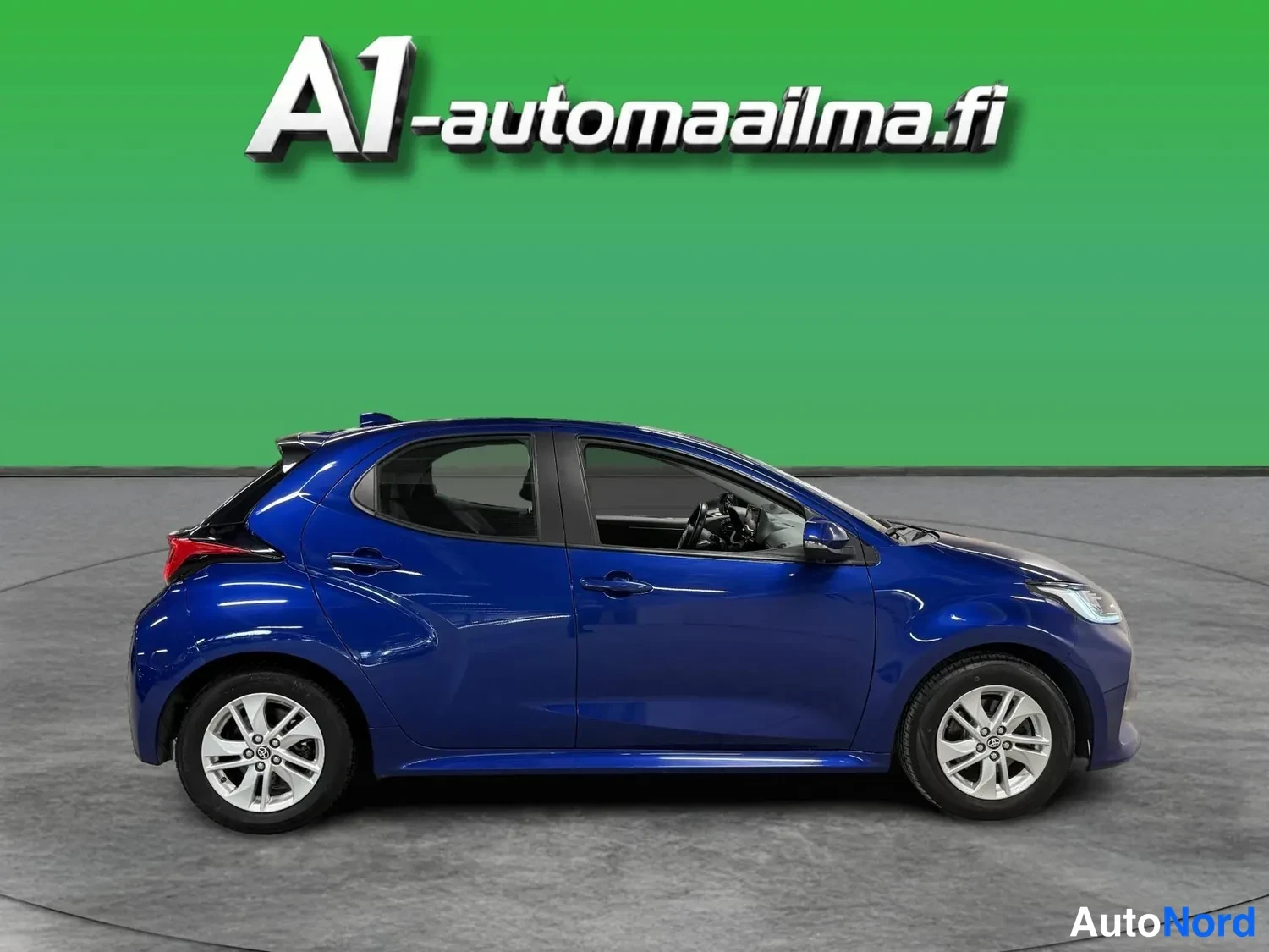 Etuviisto, nokka oikealle: Sininen Toyota Yaris kulmassa etuosasta oikealle, studiosetausta.