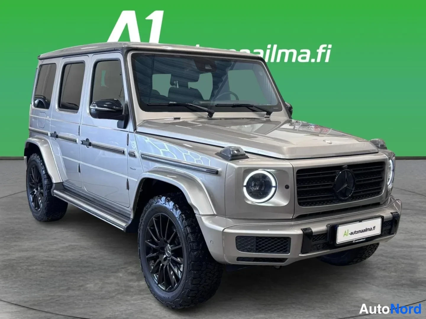 Etuviisto, nokka oikealle: Mercedes-Benz G:n etukulmakuva oikealta autosalissa: harmaa beige koripelti, LED-merkkivalot, musta etusäleikkö ja mustat vanteet.