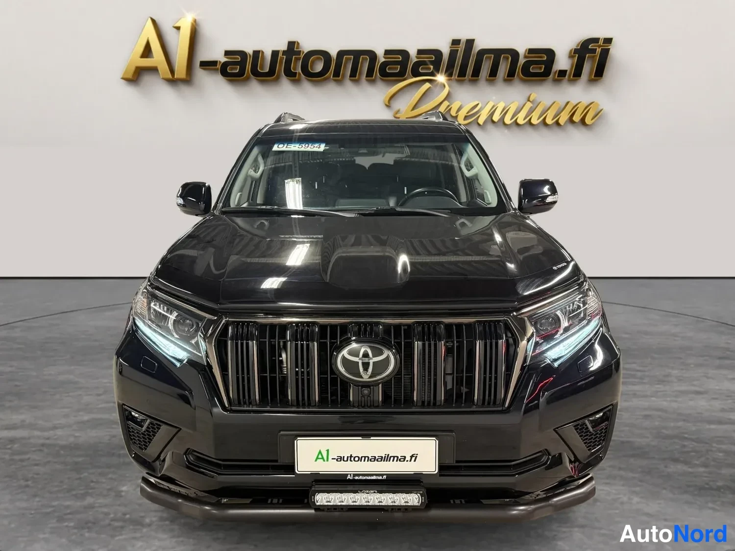 Edestä: Musta Toyota Land Cruiser suoraan edestä kuvattuna, Toyota-merkki etusäleikössä.