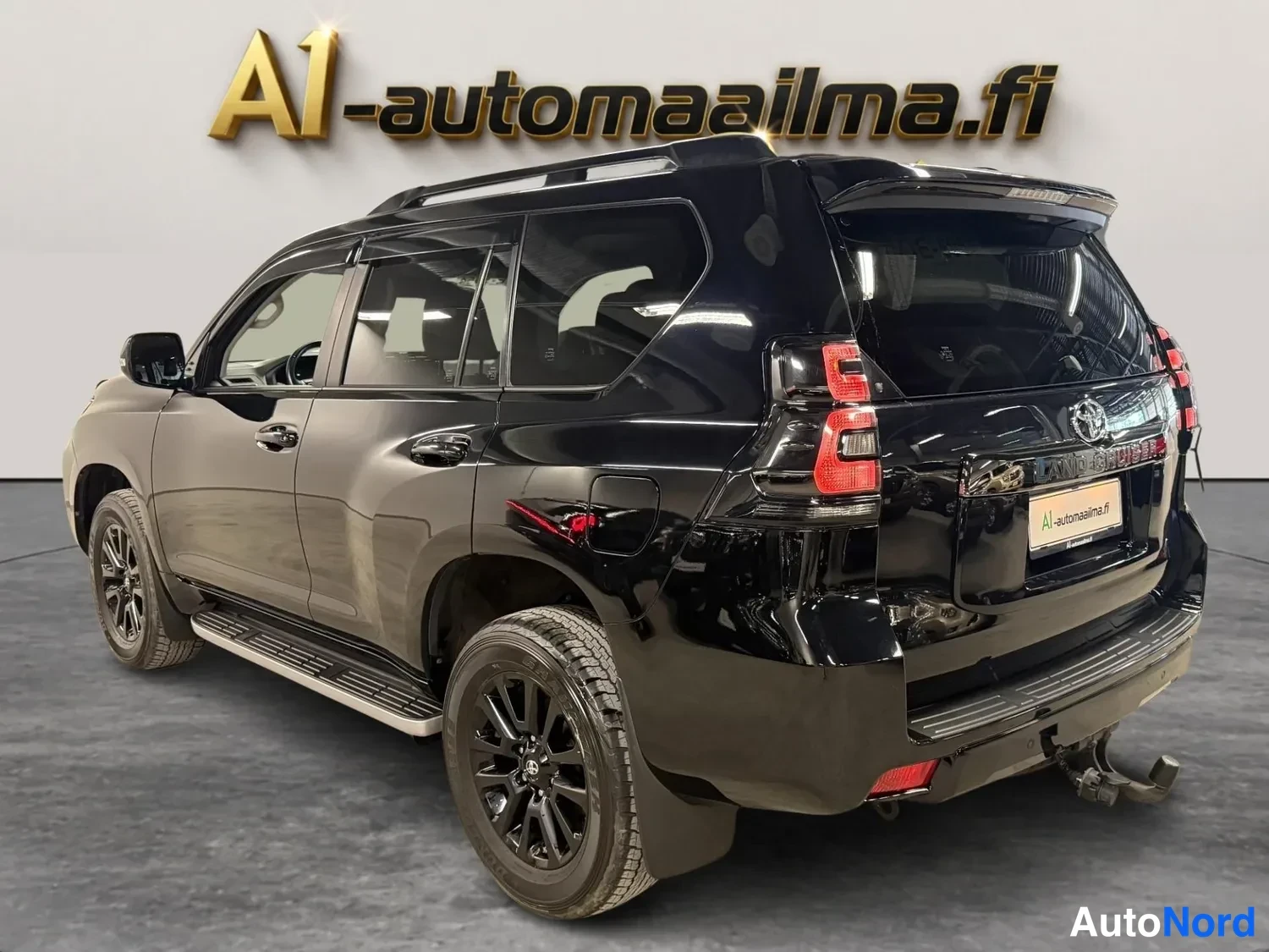 Takaviisto: Musta Toyota Land Cruiser takaa kulmasta kuvattuna, takavalot ja perävaunukytkin näkyvät.