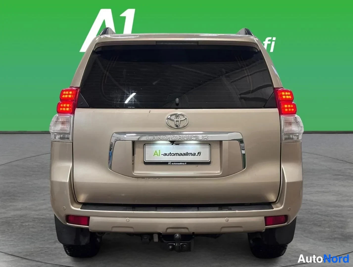 Takaa: Auton takaosa: Toyota Land Cruiser, beige-kultainen koripelti, LAND CRUISER -teksti ja Toyota-merkki rekisterikilven yllä, punaiset takavalot ja vetokoukku näky