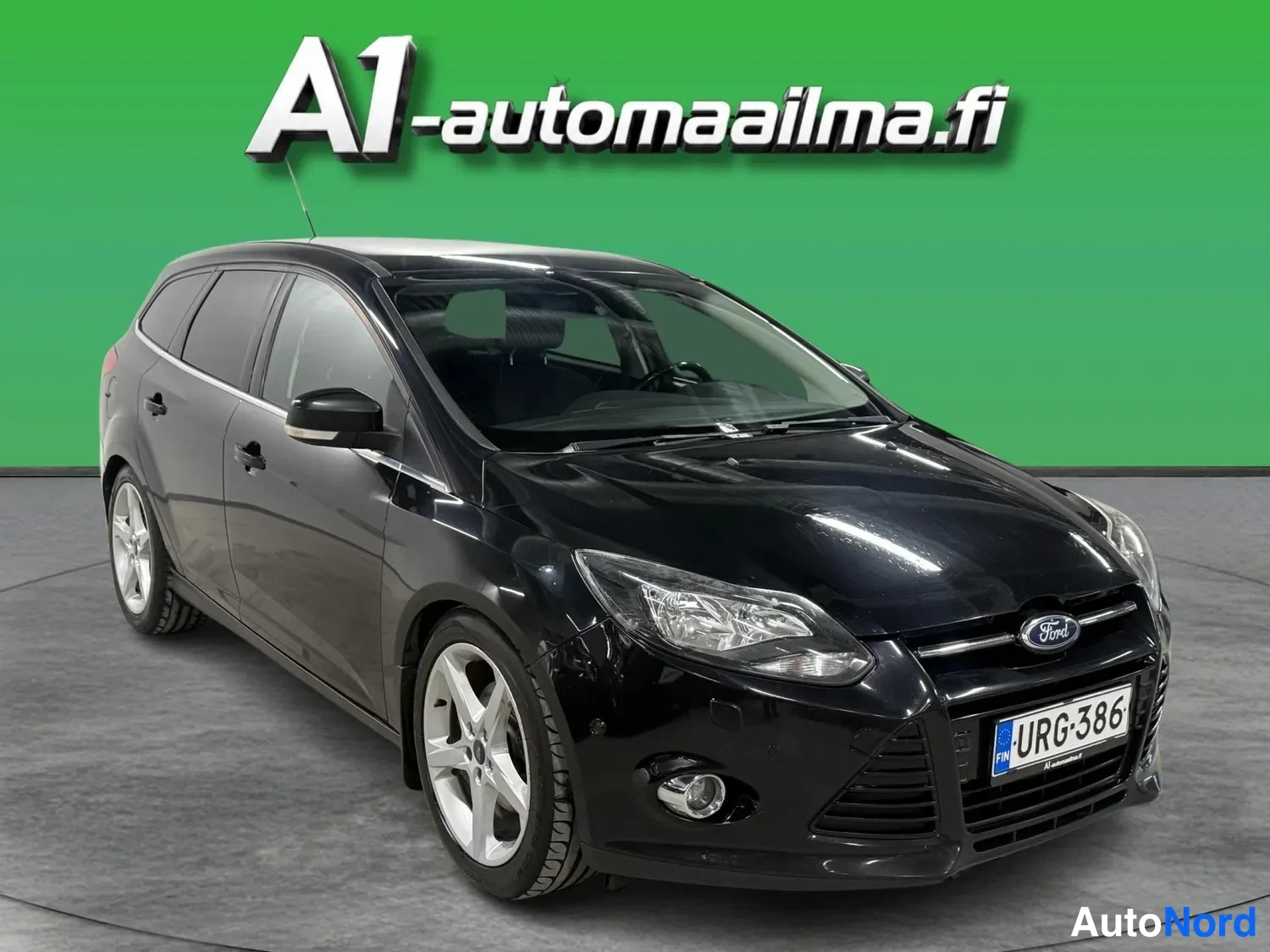 Etuviisto, nokka oikealle: Musta Ford Focus -asema-auto kolmesta neljäsosasta etuosasta oikealle kääntyneenä, rekisterimerkki.