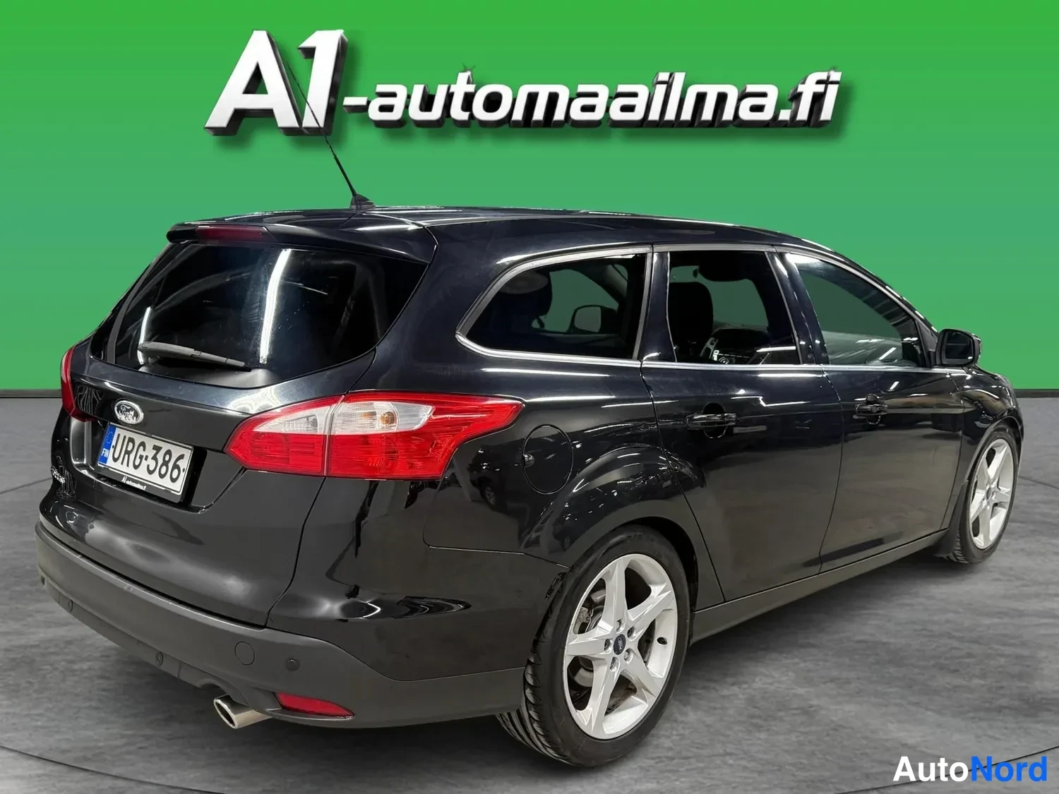 Takaviisto: Musta Ford Focus -asema-auto takaa sivulta kuvattuna, punaiset takavalot ja rekisterimerkki.