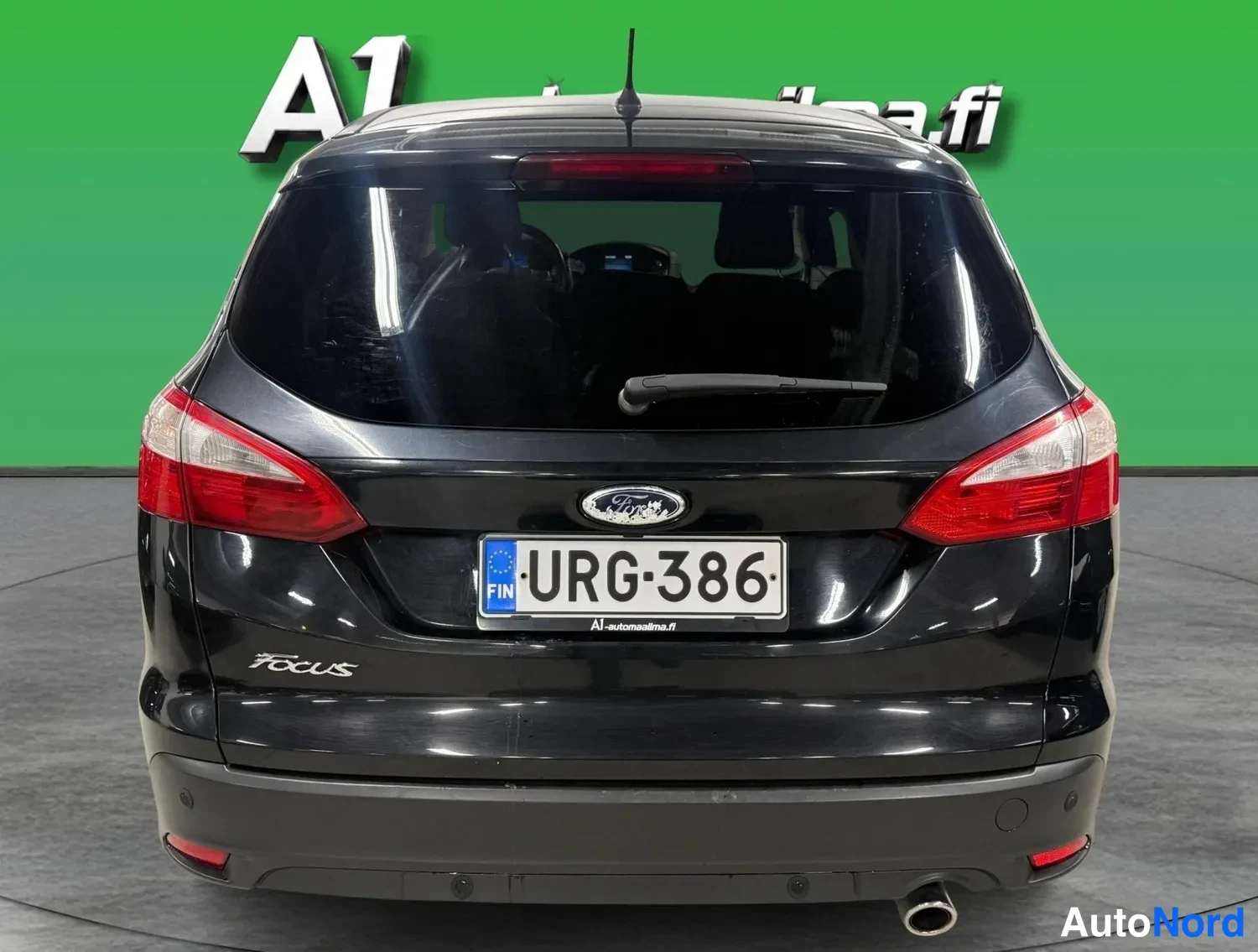 Takaa: Ford Focus -farmarin takaosan suorakuva: tummat takavalot, Ford-merkki ja Focus-teksti bootin kannessa, rekisteritunnus, musta koriväri, vihreä tausta.
