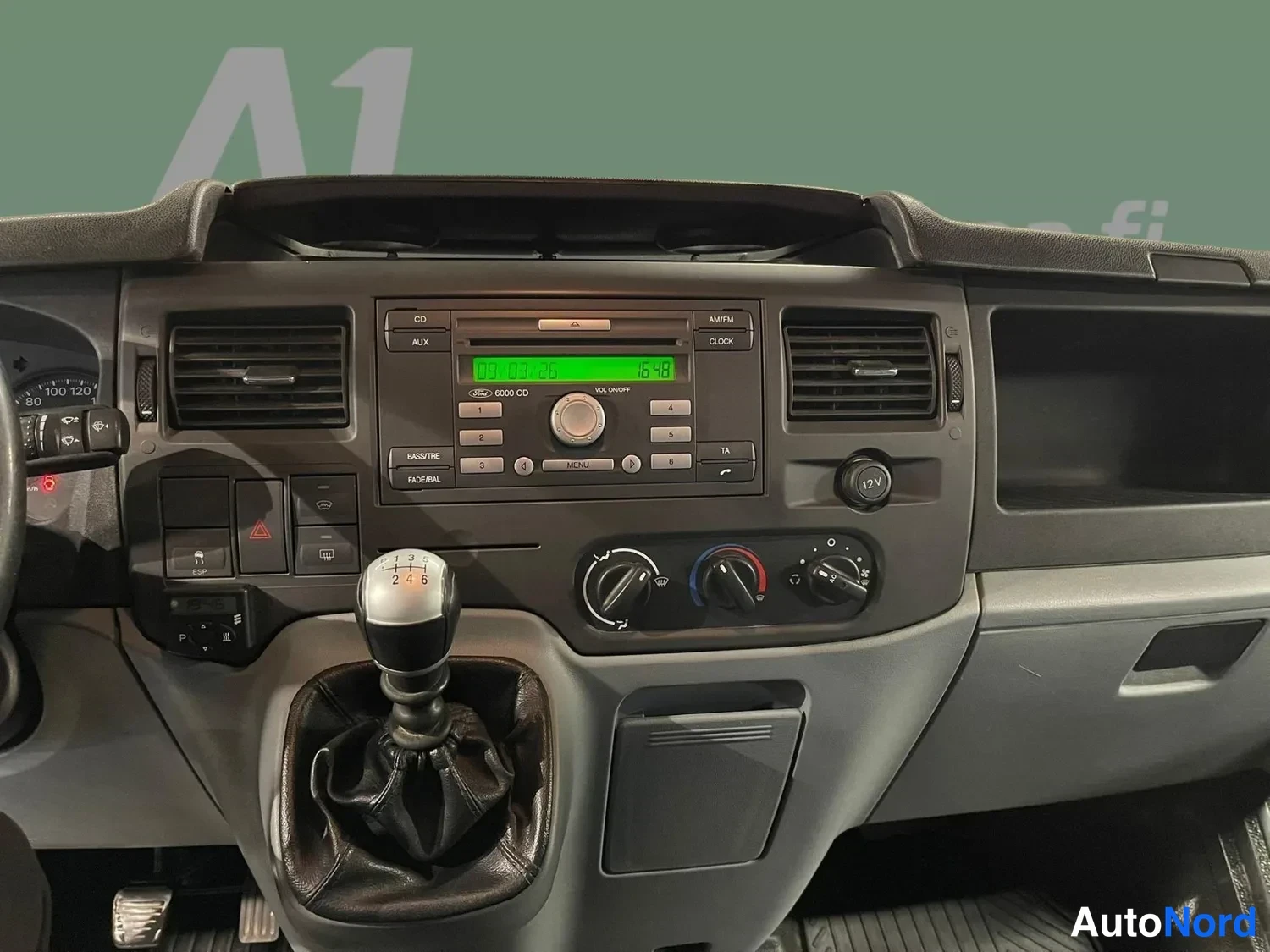 Muu: Kojelaudan keskiosa lähikuvassa: Ford 6000 CD -radio vihreällä näytöllä, manuaalivaihteiston vipu ja kahvat/ilmastointisäätimet.