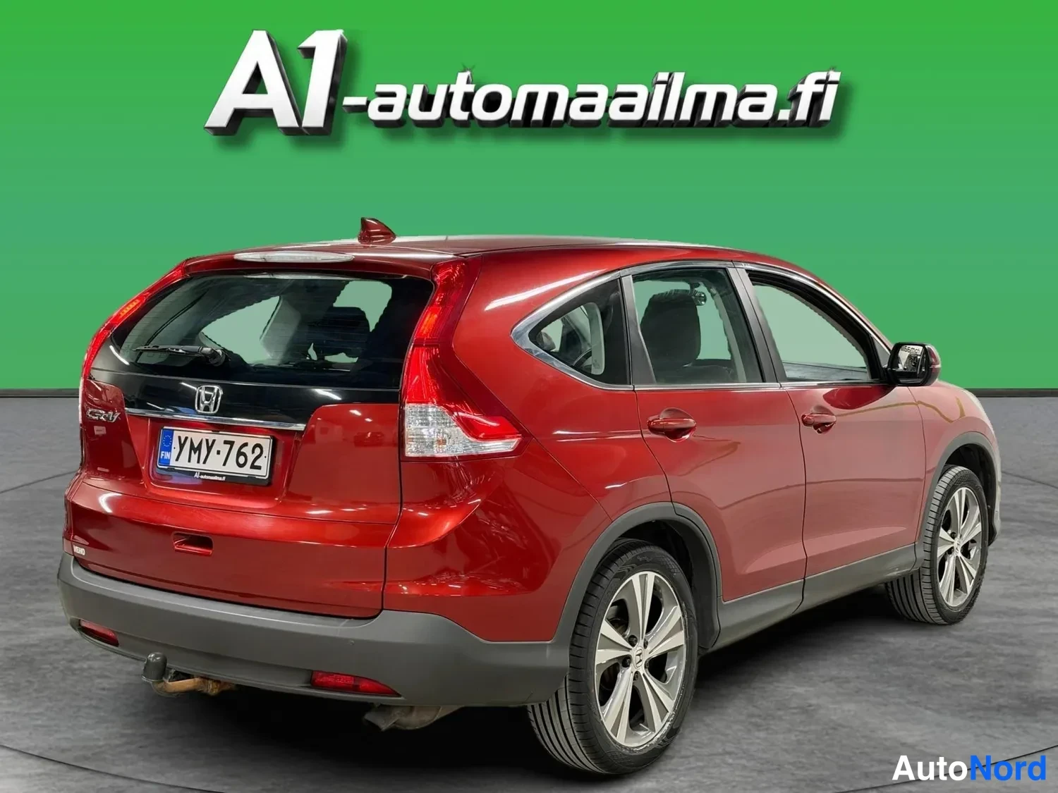 Takaviisto: Honda CR-V kulmassa takaa vasemmalta, kokonaan näkyvä punainen auto vihreää taustaa vasten.