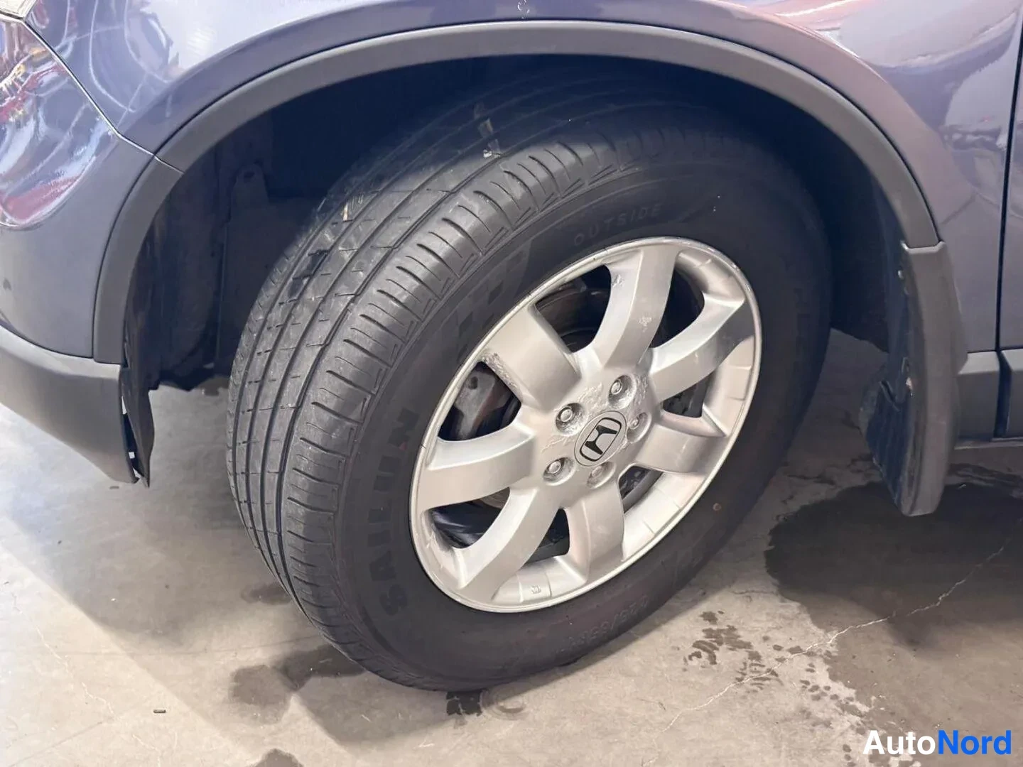 Muu: Lähikuva auton pyörästä: hopea Honda-alumiinvanne ja SAILUN-rengas, levyjarru näkyy vanteen raosta; autossa tummansininen maali ja mustat muoviset pyöräaukon re