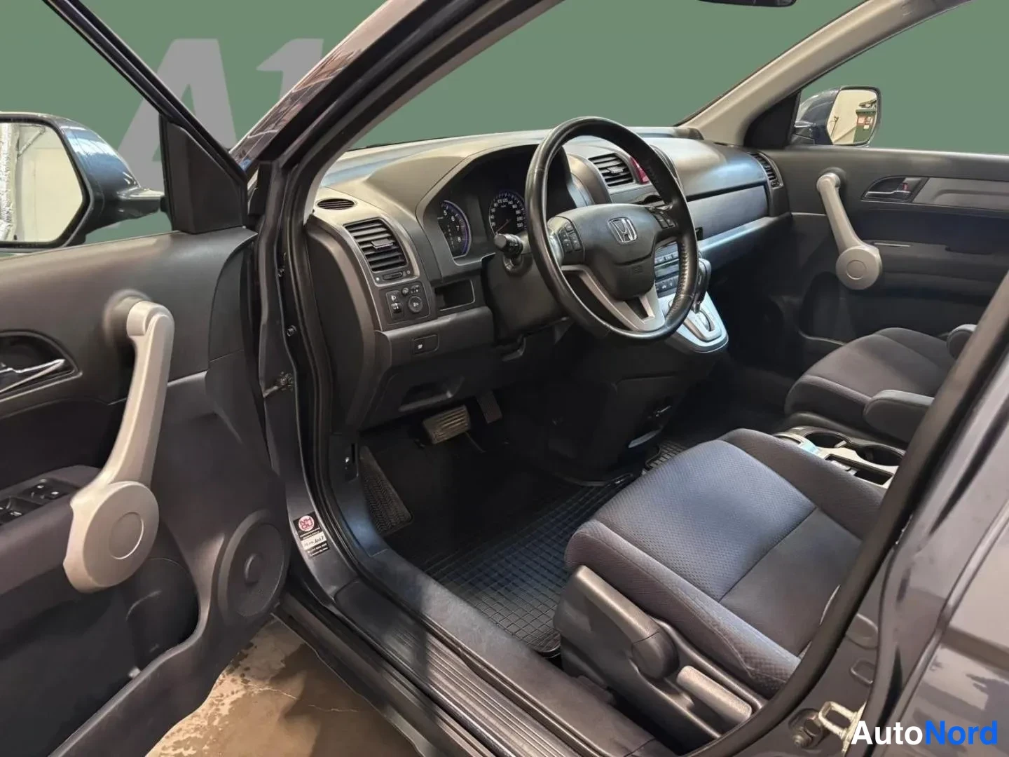 Sivulta: Honda CR-V:n etuistuin ja kojelaudan kuljettajan puoli; autohallin ympäristö, ohjauspyörä, mittaristo ja keskikonsoli.
