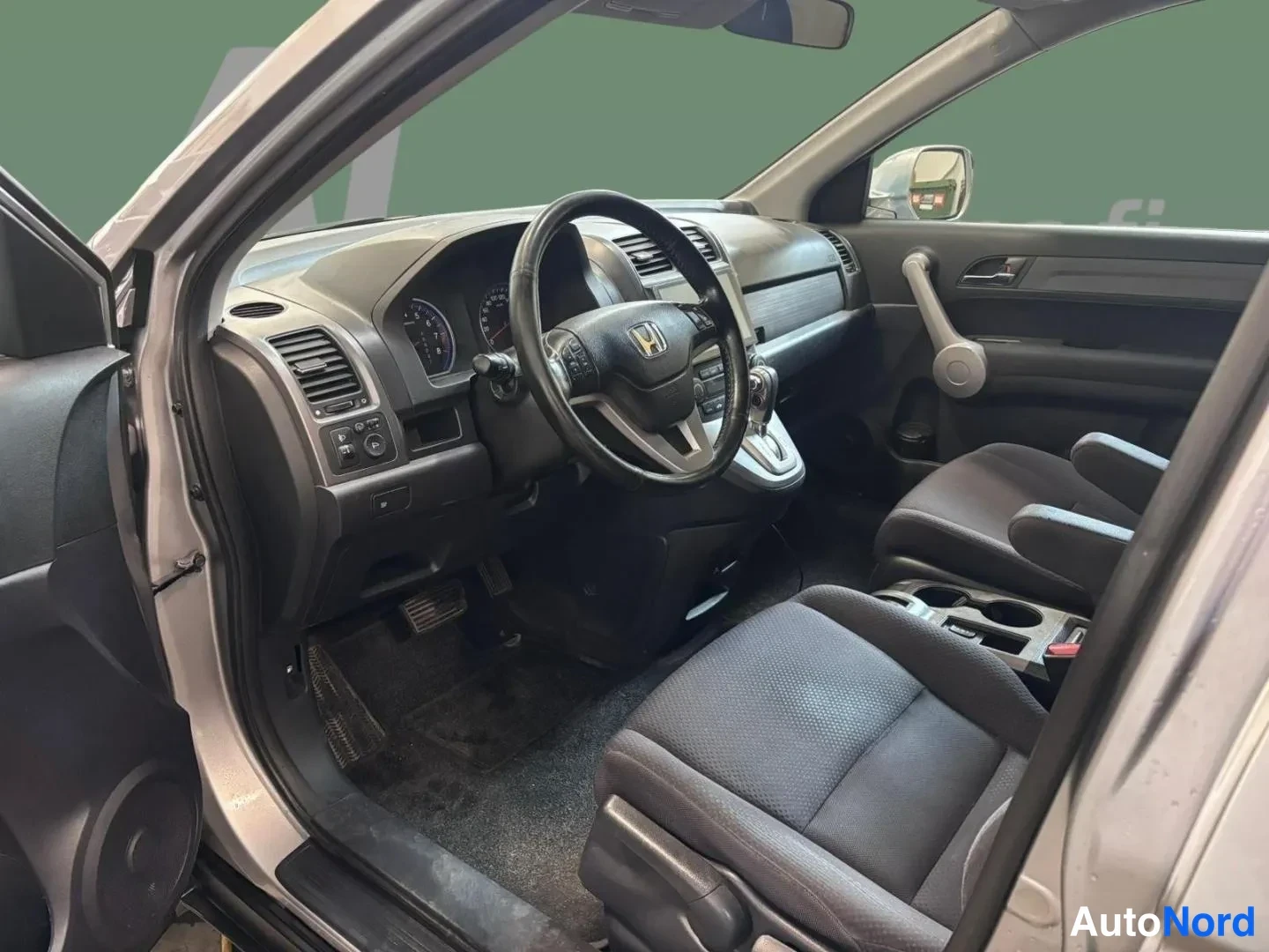 Muu: Honda CR-V:n sisätilat kuljettajan oven kautta; tumma kangasverhoilu,Honda-merkkinen ohjauspyörä, manuaali- tai automaattivaihteen valitsin keskikonsolissa ja k