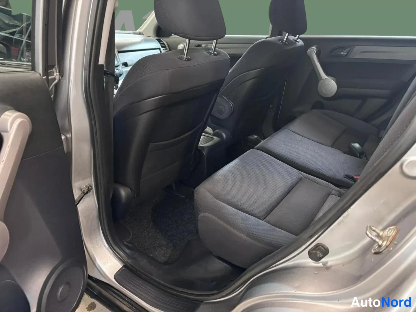 Muu: Avatusta takaovesta kuvattu Honda CR-V:n takapenkki ja matkustamo: tummansävyinen kankiverhoiltu takapenkki, etuistuinten selkänojat ja lattiamatto näkyvät.