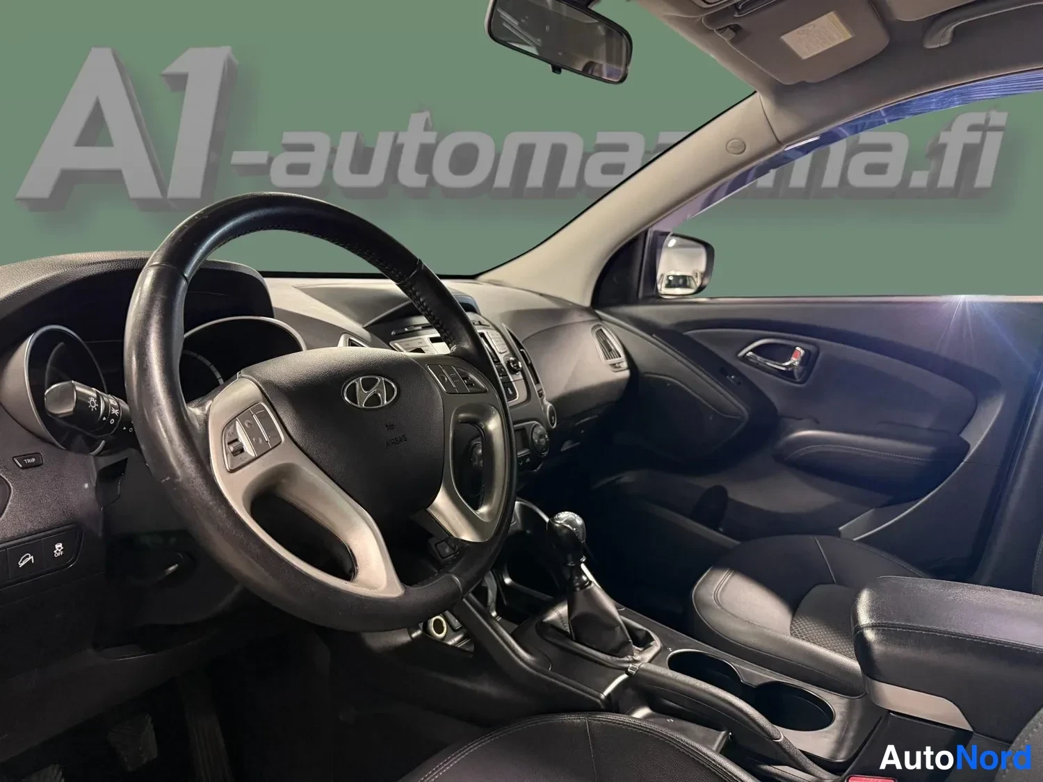 Muu: Hyundai ix35:n ohjaamo: Hyundai-ohjauspyörä, manuaalivaihteiston vaihtokeila ja keskikonsoli.