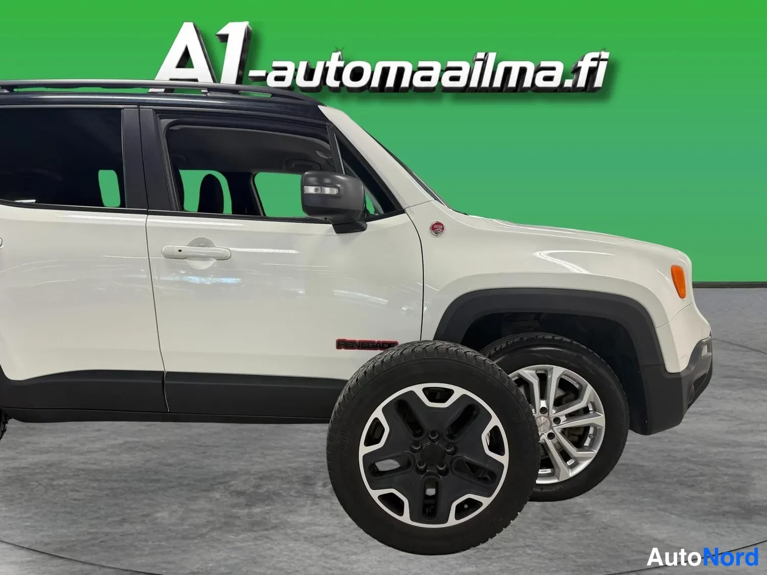 Sivulta: Valkoisen Jeep Renegade -maasturin kylkikuva, kattokaiteet ja hopeat kevytmetallivanteet näkyvissä, etualalla irrallinen rengas.
