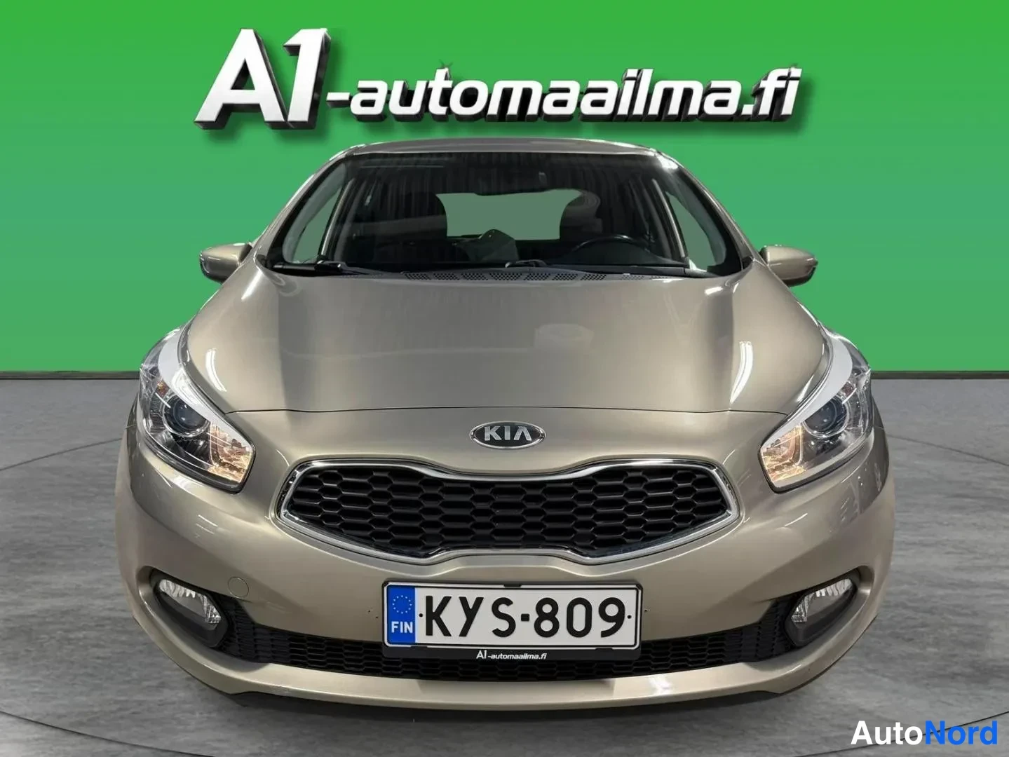 Edestä: Kia Ceed -auto suoraan edestä, beige-hopeinen etunäkymä studiovihreällä taustalla