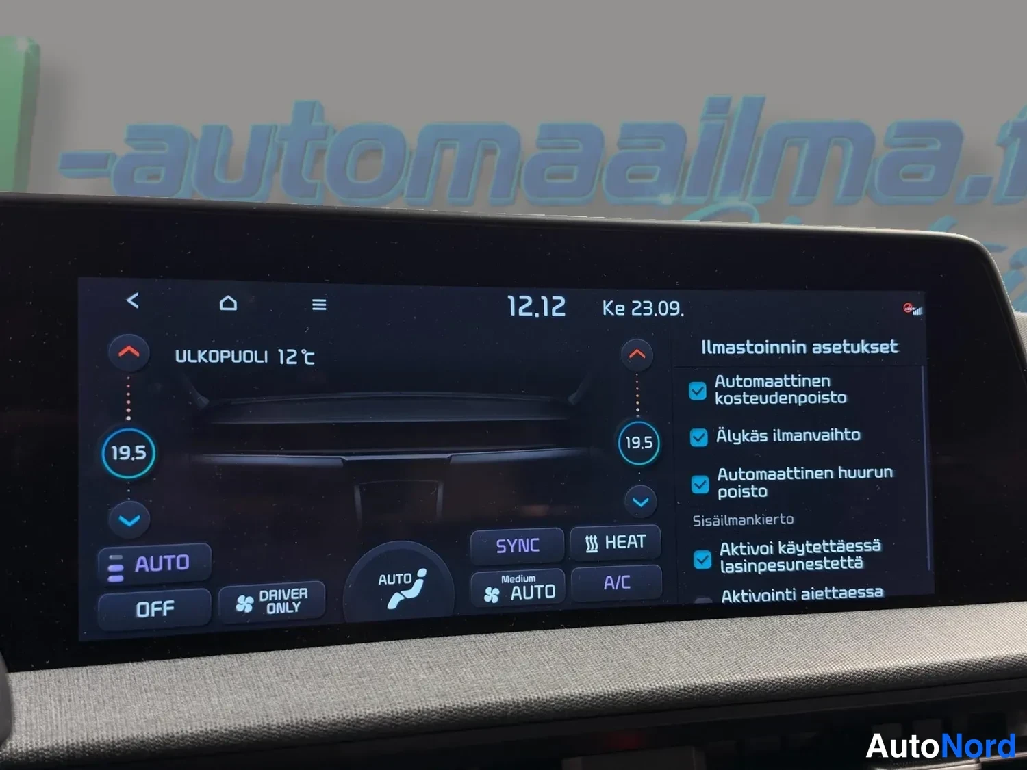 Yksityiskohta: Istuttokuvan infotainment-näyttö, jossa ilmastoinnin asetukset: molempien sivujen lämpötila 19,5 °C, ulkolämpötila 12 °C sekä valikot automaattiselle kosteudenp