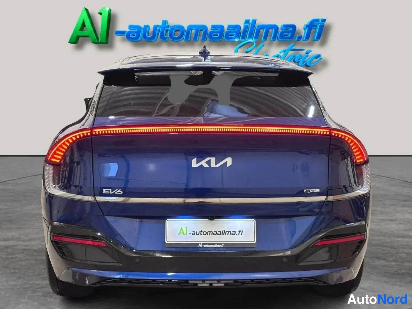 Takaa: Sininen Kia EV6 takaa kuvattuna, punainen valojohteinen takavalo koholla, Kia-merkki ja EV6-teksti rekisterikilven yllä.