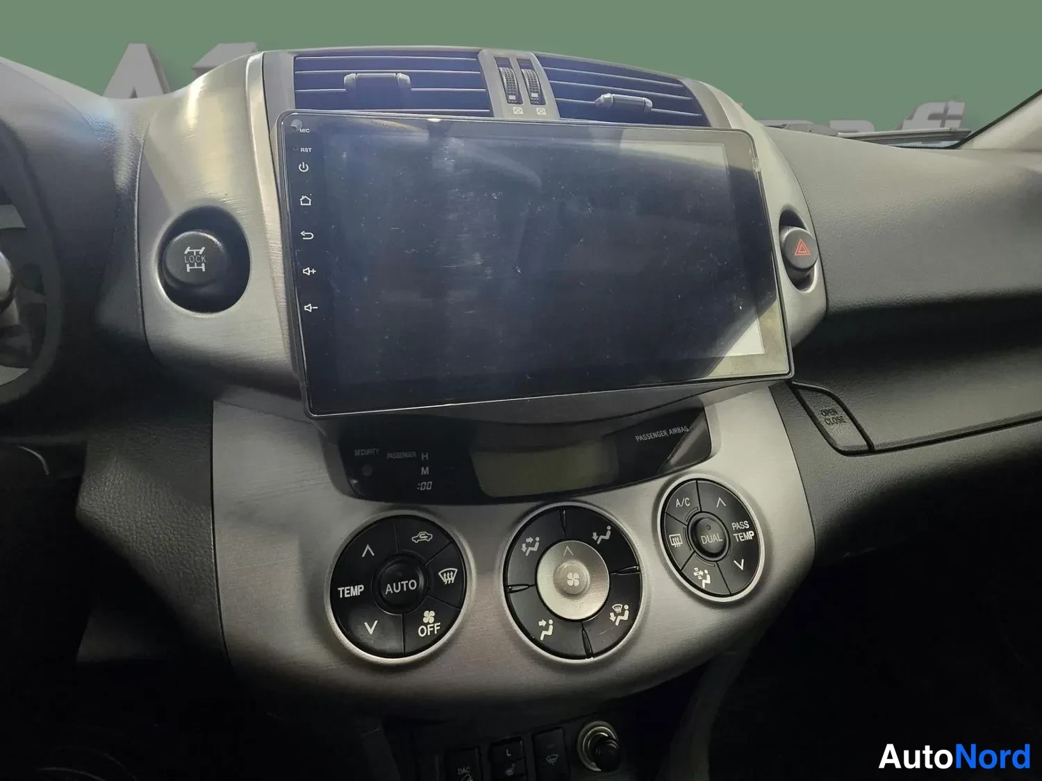 Sivulta: Kojelaudan keskiosa: infotainment-näyttö keskellä, automaattinen ilmastointi (AUTO, A/C, DUAL) -säätimet javaroitusmerkin painike.