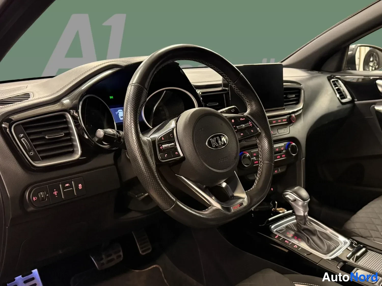 Edestä: Ohjaamo vasemmalta kuvattuna: Kia-merkkinen multifunktiohirsi, automaattivaihtehan vivustoineen, nappihallintaa ja kojetaulu.