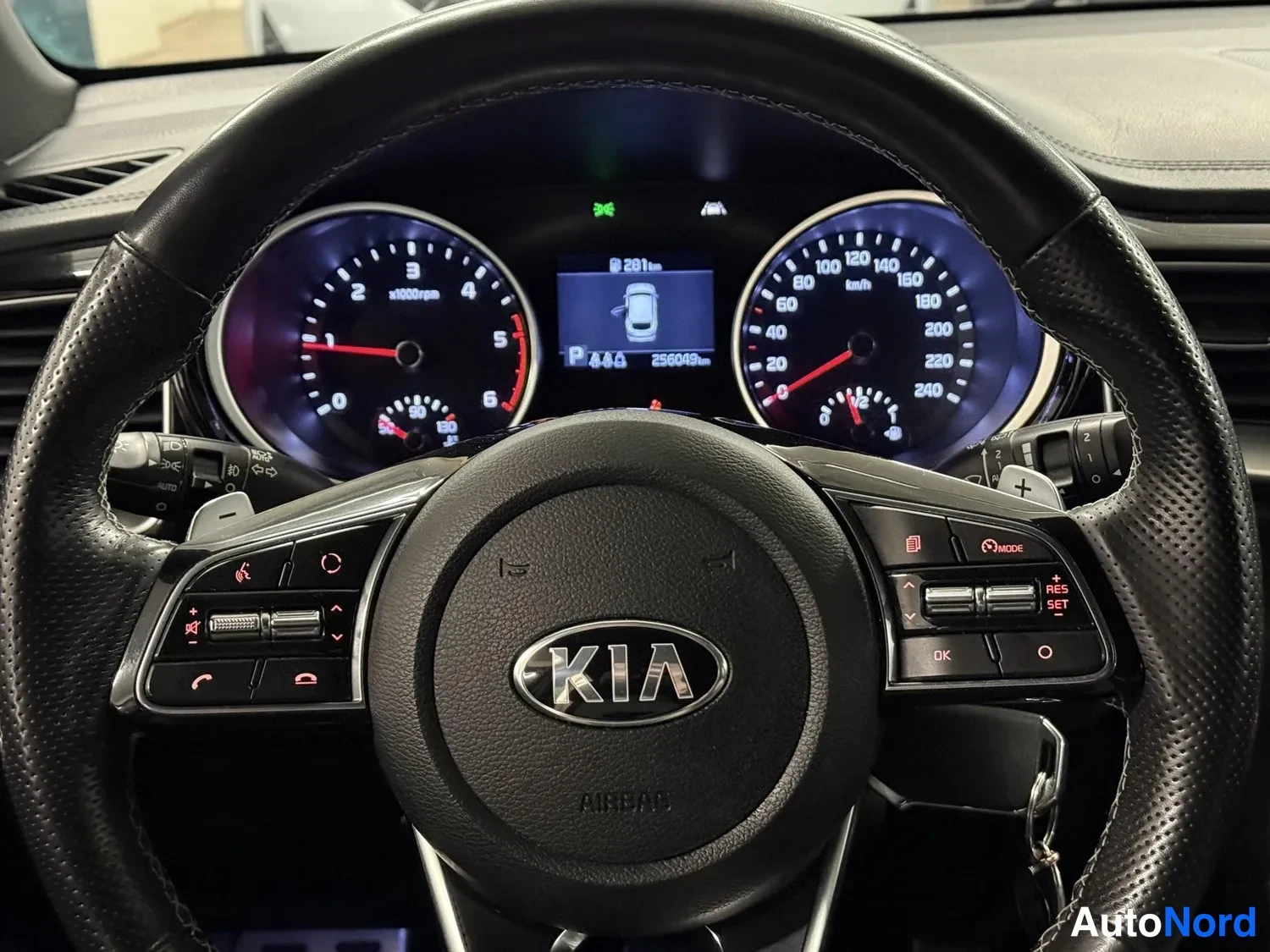 Edestä: Rattitilanne suoraan edestä: Kia-merkitty ohjauspyörä, analogiset mittarit ja näytöllä lukema 256049 km sekä vaihteen P.