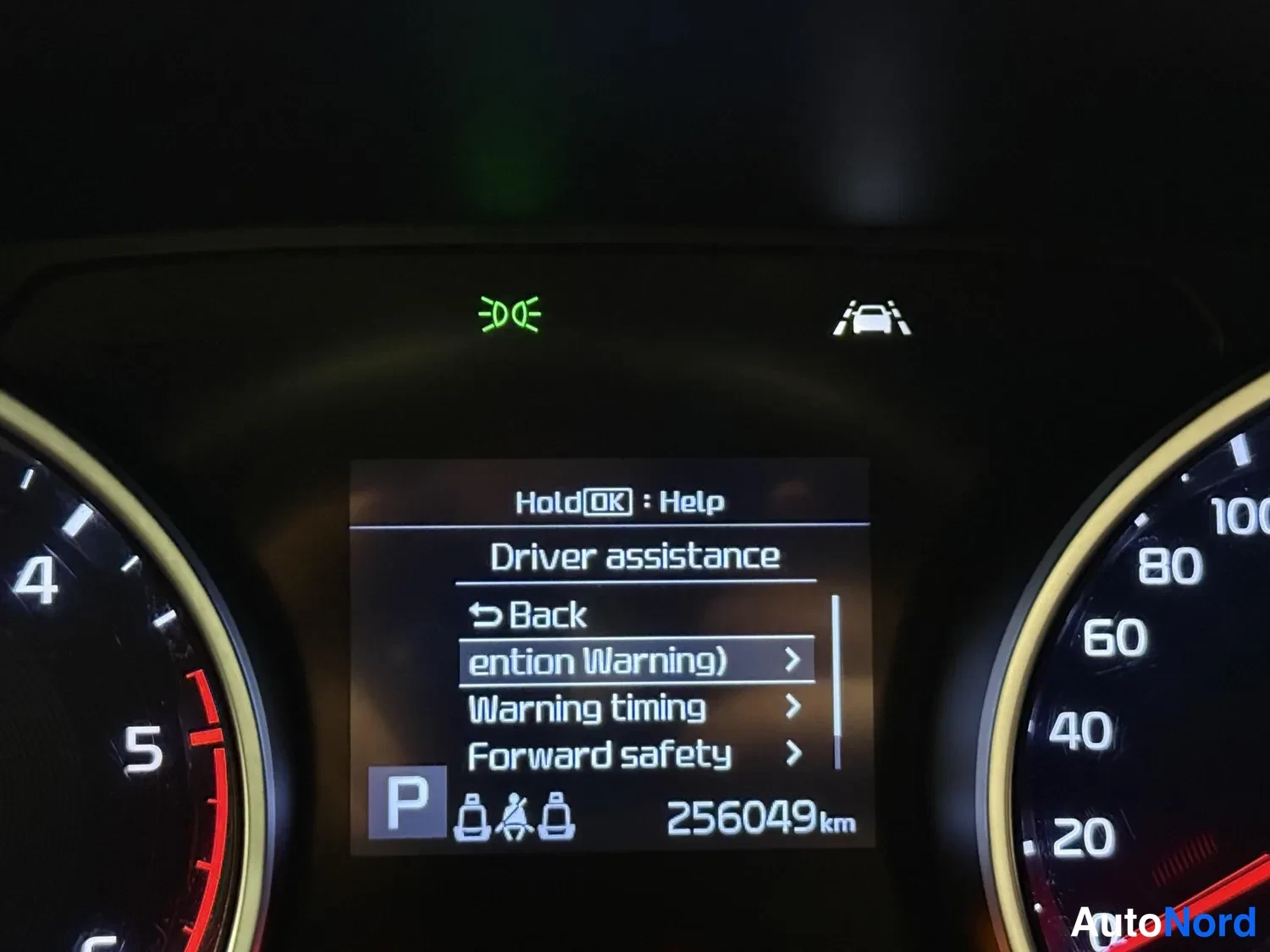 Yksityiskohta: Kojeiston tiedot näkyvät kuvassa: ajovalot, kaistavahti, P-parkkitila, 256049 km, mittarit 0–100 ja 0–5, Driver assistance -valikko.