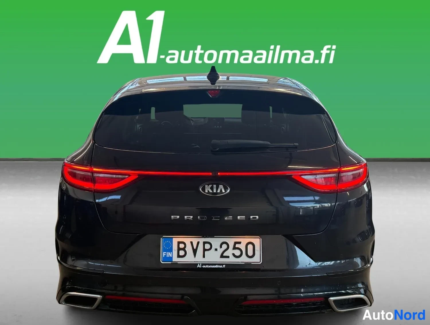 Takaa: Mustan Kia ProCeedin takanäkyjä: KIA-merkki, PROCEED-teksti, punaiset takavalot, rekisterikilpi ja kaksoispakoputket.