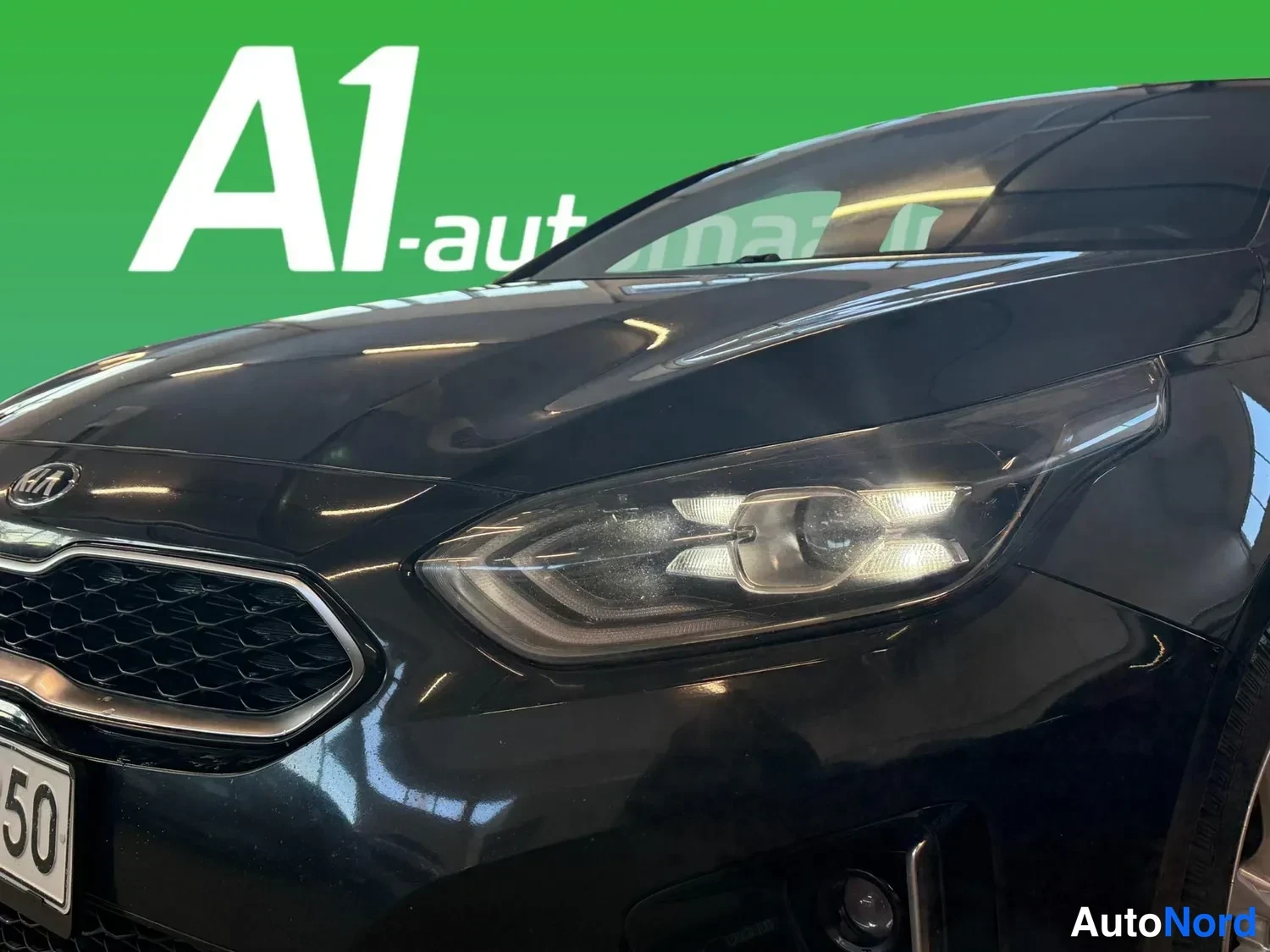 Edestä: Lähikuva mustan auton etuosasta: KIA-merkki, verkkokateinen etusäleikkö ja etuvalo.