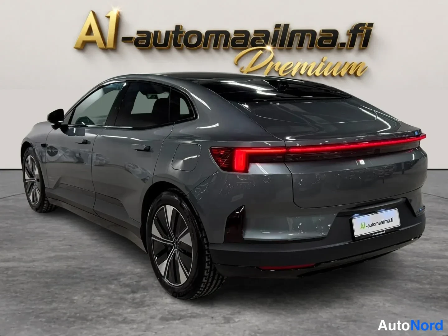 Takaviisto: Auto takaapäin hieman sivusta: tummanharmaa coupe-tyylinen korimalli, täysleveä punainen takavalo ja musta lasikatto.