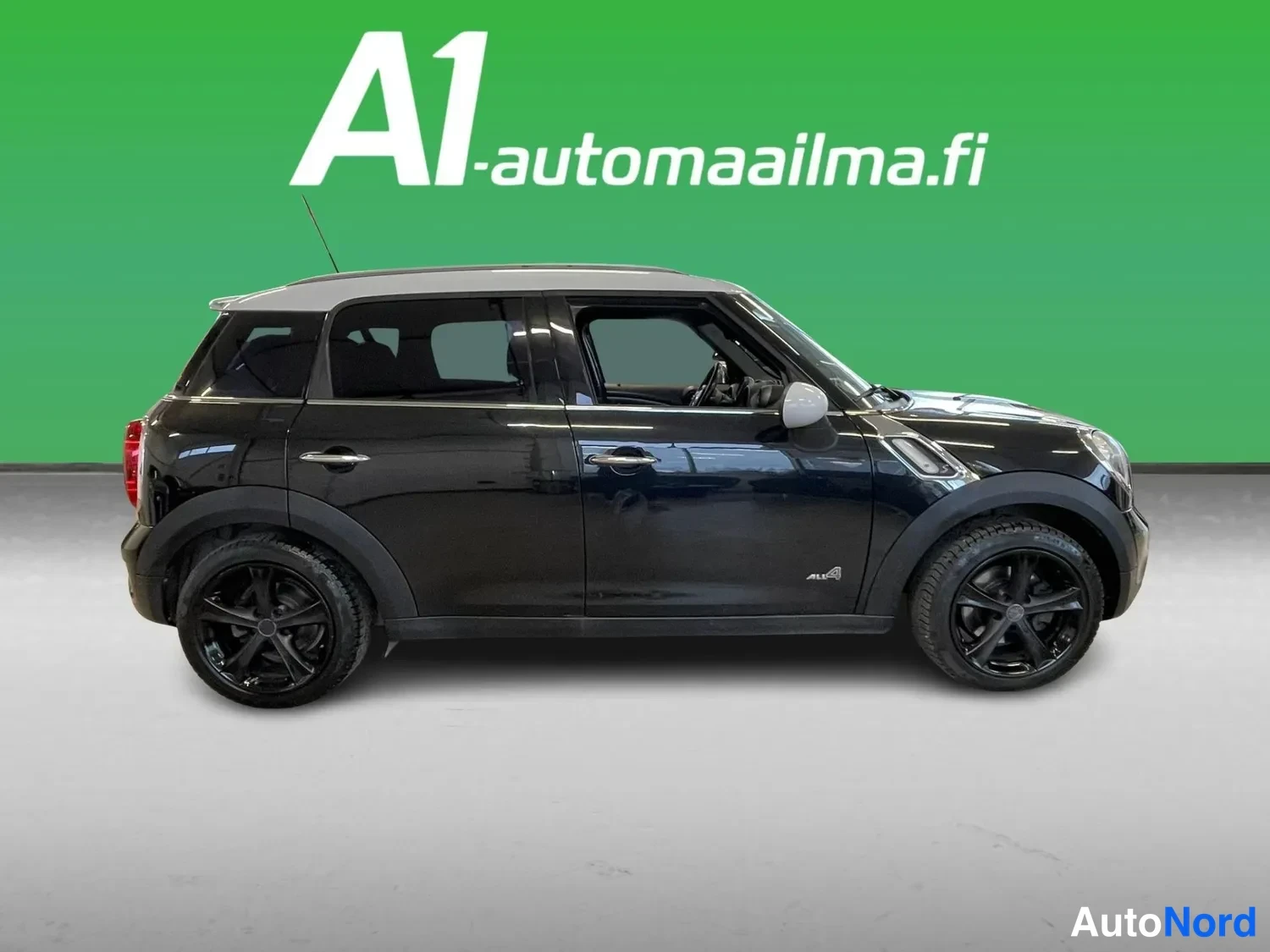 Sivulta: Mustan Mini Countrymanin sivunäkymä oikealta puolelta, katettu valkoinen katto ja mustat kevytmetallivanteet.