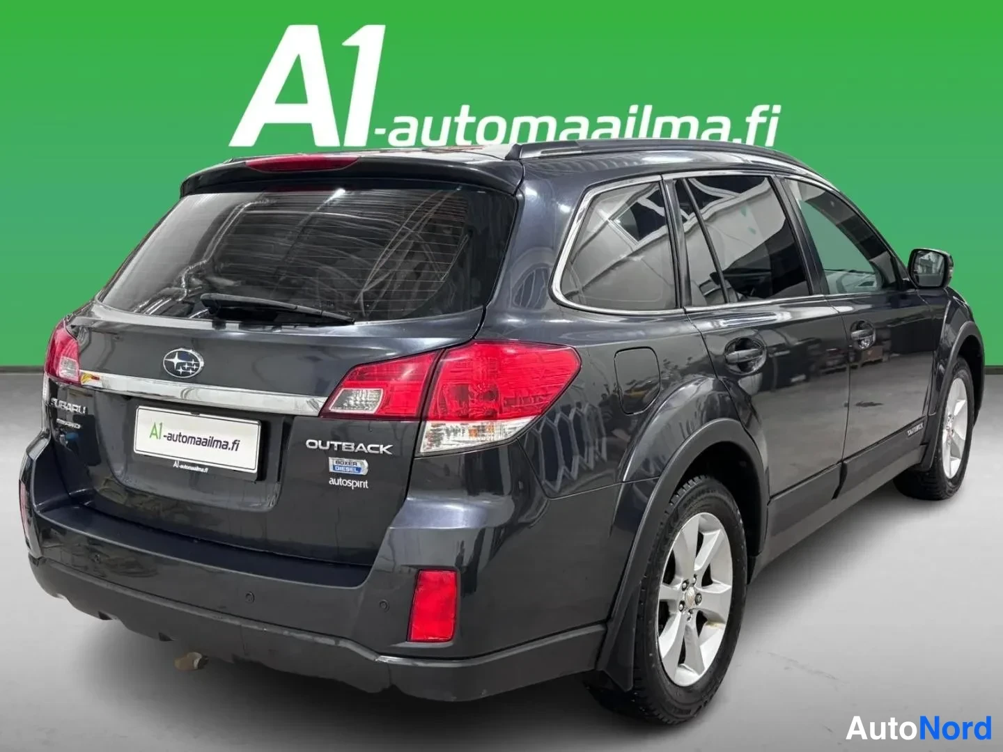 Takaviisto: Tummanharmaa Subaru Outback -farmari takaviistosta kuvattuna, takavalot,OUTBACK-merkintä ja A1-automaailma.fi-kilpi näkyvät.