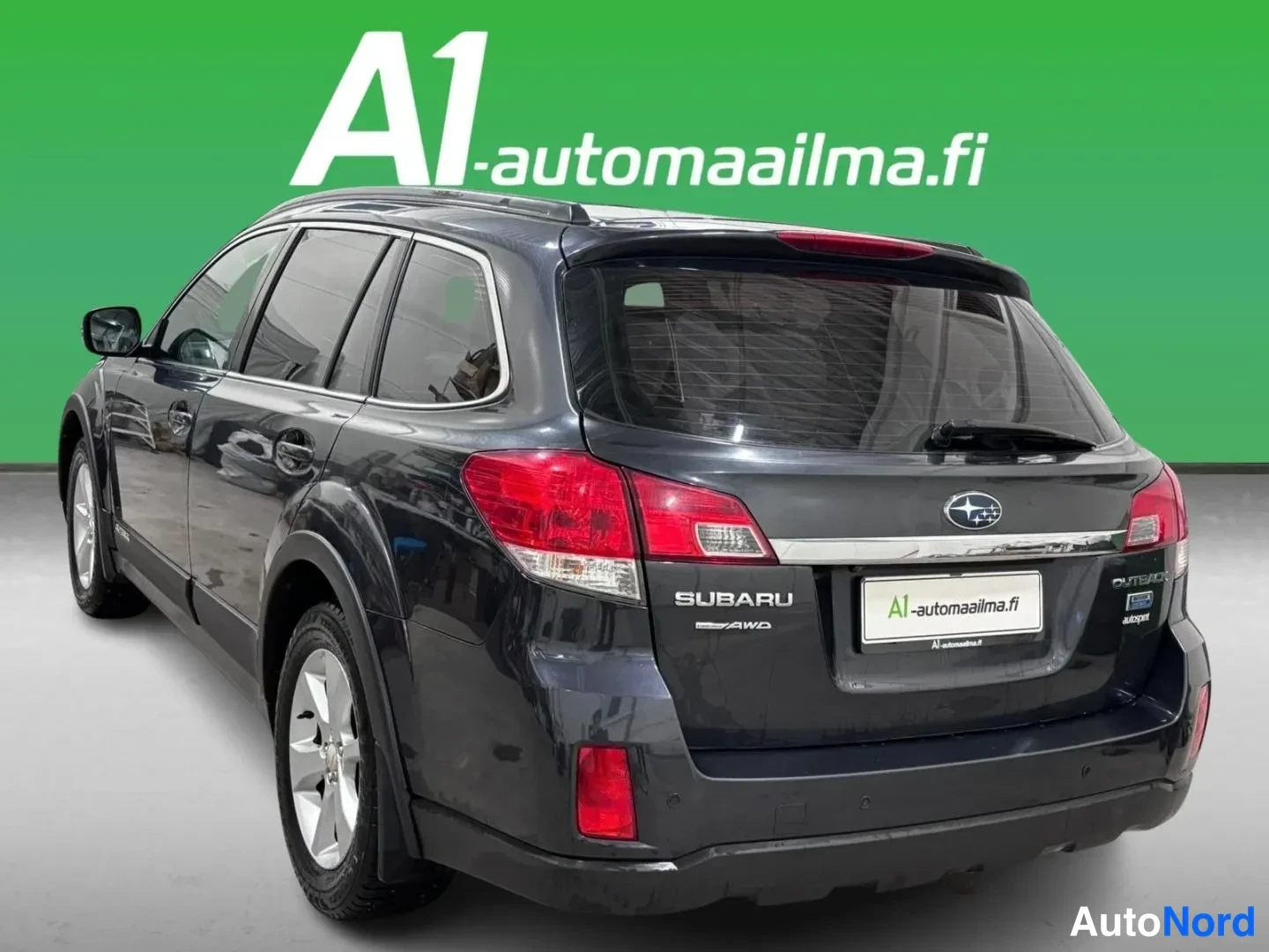 Takaviisto: Tummanharmaa Subaru Outback -farmari takaviistosta kuvattuna vasemmalta; takavalot, SUBARU AWD -merkintä ja kattokaiteet näkyvät.