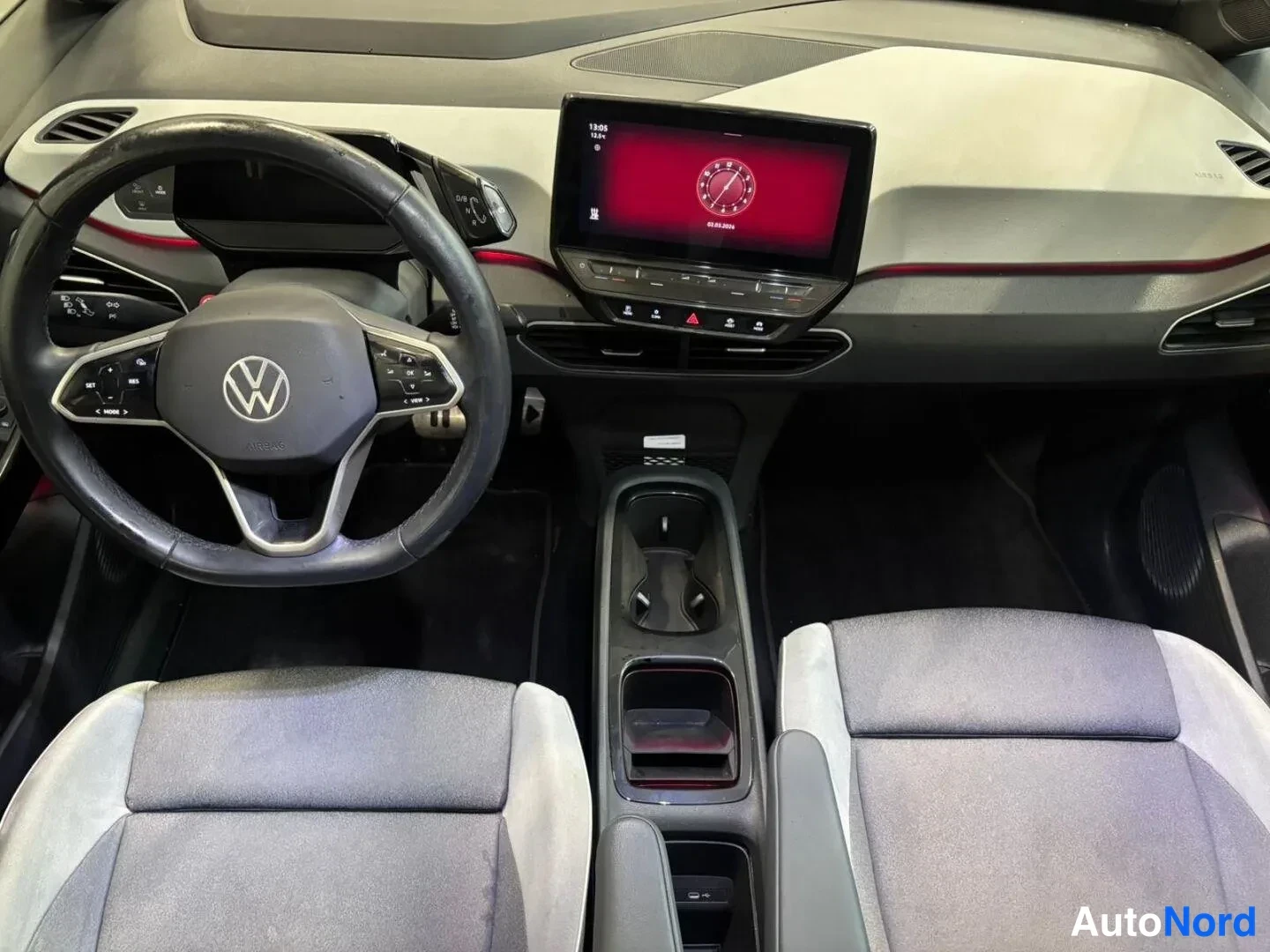 Muu: Ohjaamo näytettävä ylhäältä: Volkswagen-ohjauspyörä, keskellä kosketusnäyttö punaisella näytöllä, kaksi harmaata etuistuinta ja keskitunneli.