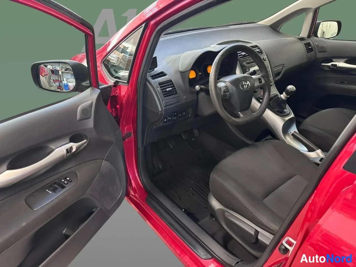 Yksityiskohta: Punaisen Toyota Auriksen etuistuin ja kojelauta vasemmalta avatusta etovest liittyen; kaksiohenkinen ratto, käsijarru, automaattivaihto kytkinpolkimien ja vaiht