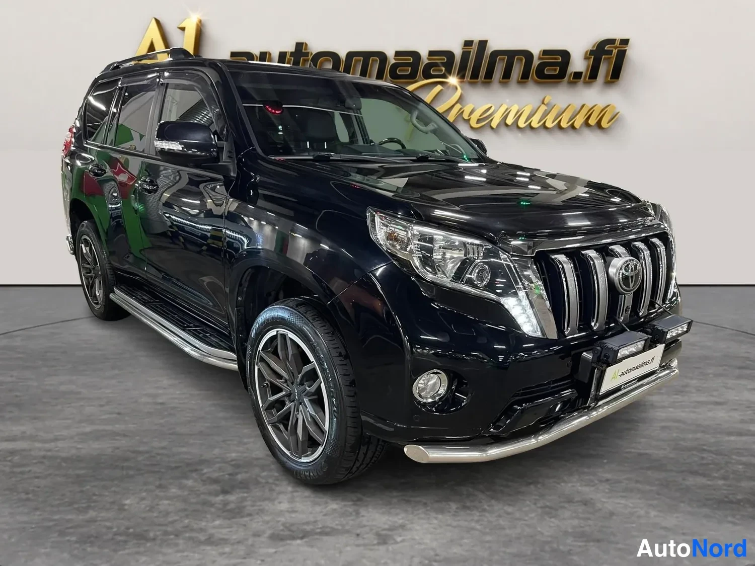 Etuviisto, nokka oikealle: Mustan Toyota Land Cruisern etukulmanäyttö oikealta, kiiltävä musta koripinta, kattotelineet ja läpinäkyvät deflektorit ovien yläpuolella.