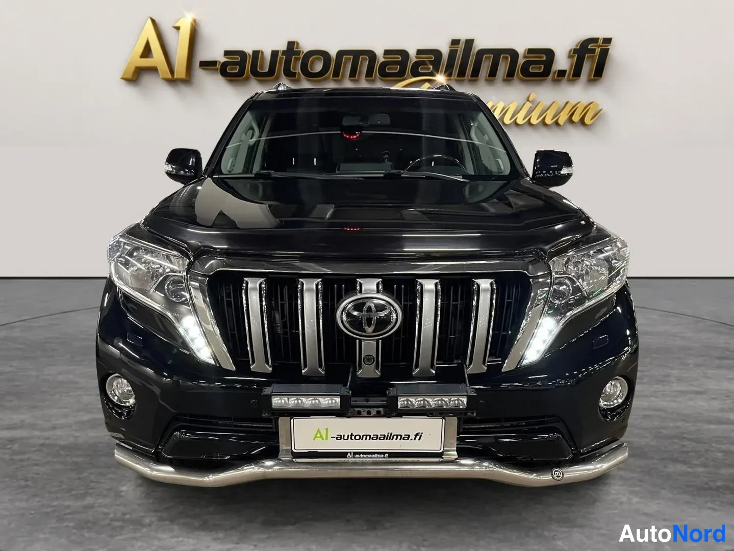 Edestä: Mustan Toyota Land Cruisern suora etunäkymä, suuret kattoteräkset ja matala etulipupuskurin etuvakotelineet etupuskurin alapuolella.