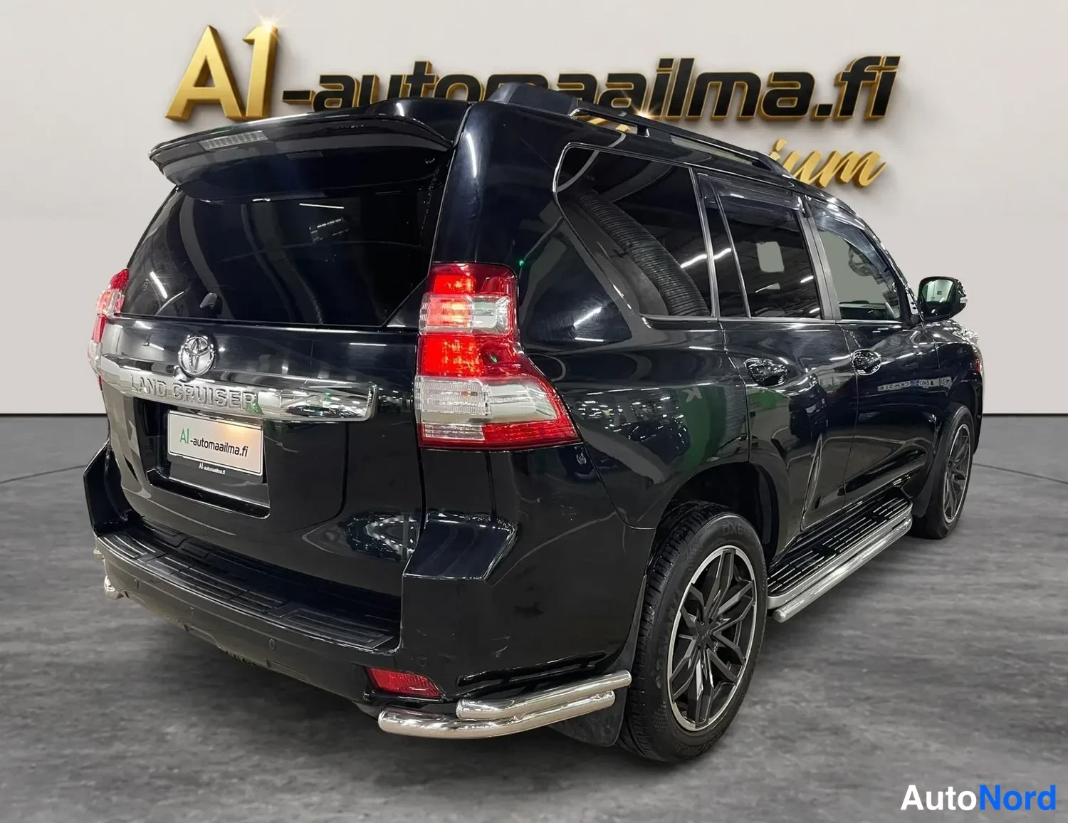 Takaviisto: Mustan Toyota Land Cruisern takaosan etukulmanäyttö vasemmalta, kattotelineet ja palkit näkyvät taustalla.