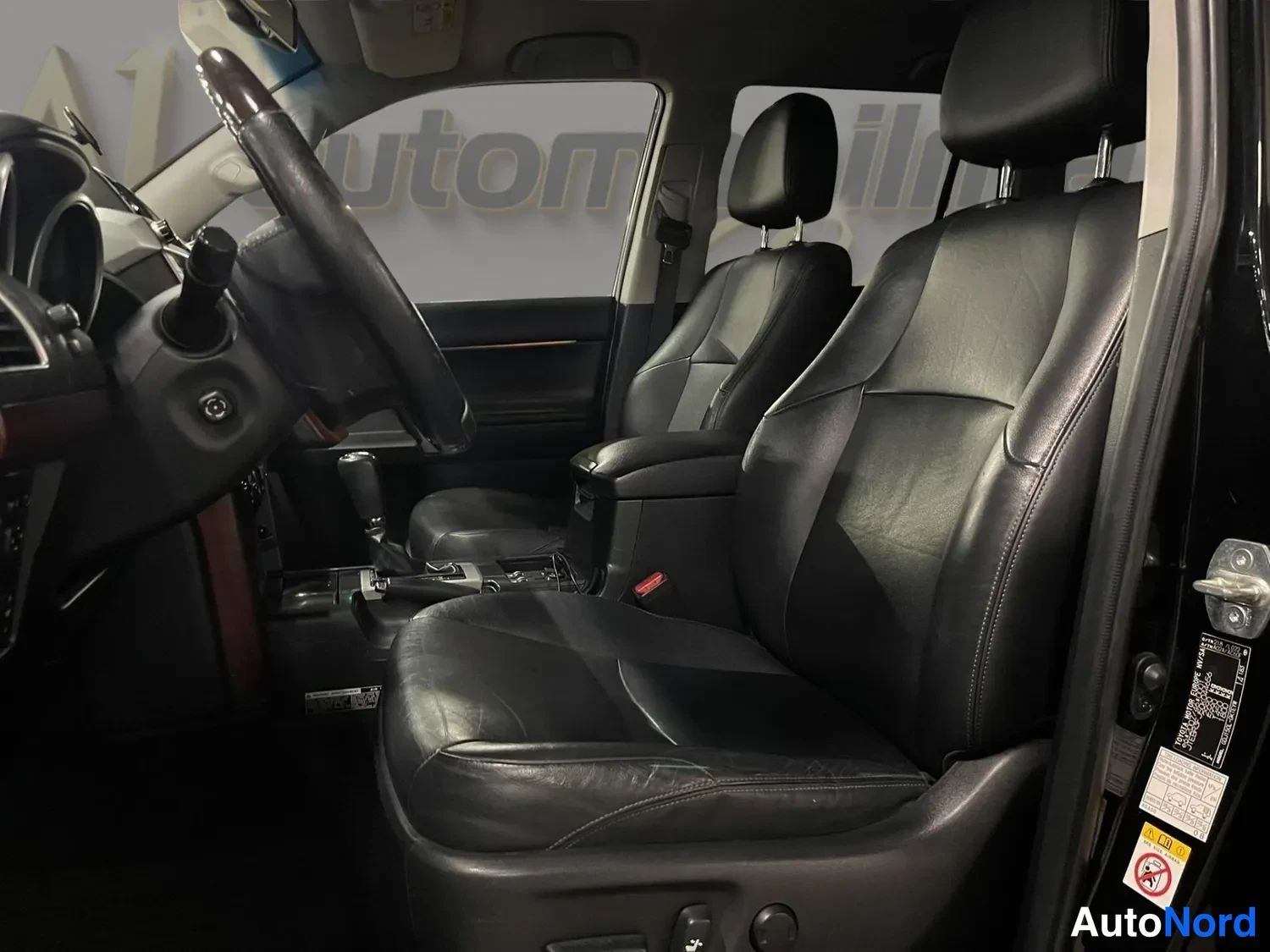 Muu: Toyota Land Cruisern etusohvan ja kuljettajan penkin mustat nahkapenkit, ohjauspyörä ja osa kojelaudasta kuvattuna ovenkauksesta.