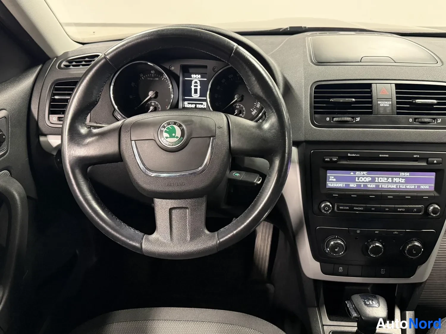 Muu: Ohjaamo näkyy kuljettajan puolelta: Skoda-merkkinen ohjauspyörä, kojelaudan mittarit, keskusnäyttö ja radio, jonka näytöllä lukee LOOP 102.4 MHz. Automaattivaih