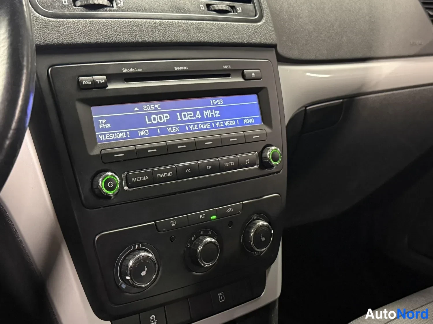 Muu: Lähikuva keskikonsolin radioista ja ilmastoinnin säätimistä. Radion näytöllä lukee LOOP 102.4 MHz ja lämpötila 20,5 °C, ja AC-painike on kuvattu.
